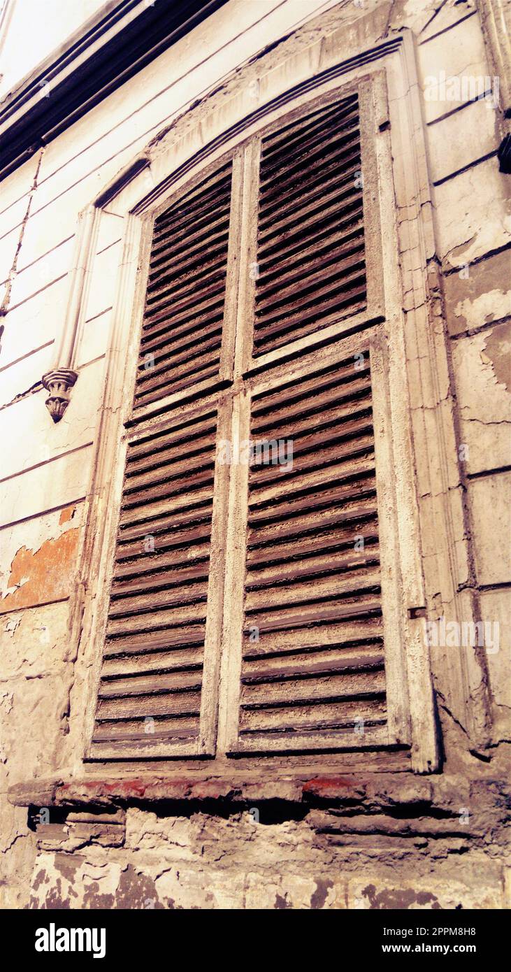Volets fermés sur une haute fenêtre avec platbands. La façade du bâtiment qui n'a pas été réparée depuis longtemps. Peler le plâtre sous la fenêtre. L'architecture de la vieille ville européenne. Banque D'Images