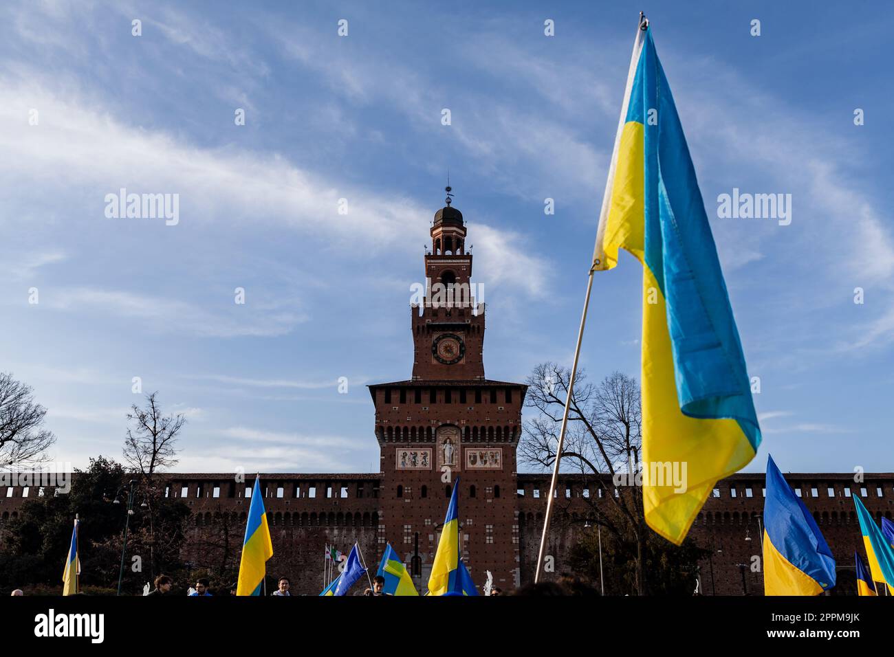 Drapeau aux couleurs rayées jaune et bleu de l'Ukraine agitant dans le vent avec un ciel bleu et le soleil. En arrière-plan le Castello Sforzesco à Milan. Banque D'Images