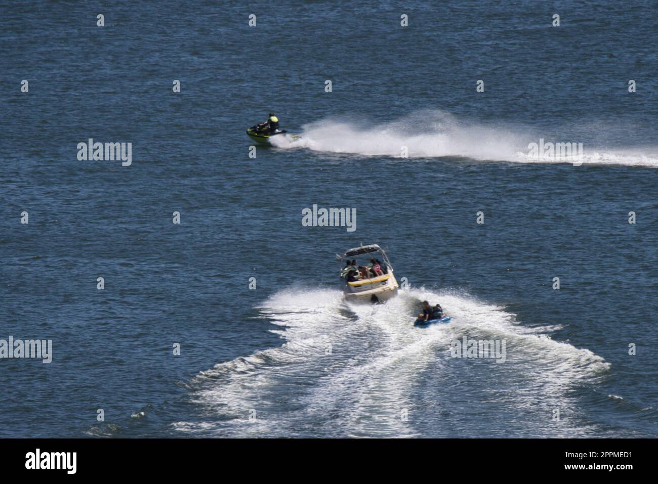 Un jetski zoome sur la surface d'un plan d'eau bleu étincelant, avec un bateau remorquant un gonflable en arrière-plan Banque D'Images