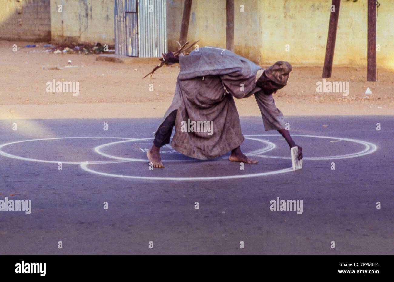 Sénégal, une personne atteinte de maladie mentale dessine des cercles sur la surface de la route dans la capitale Dakar Banque D'Images