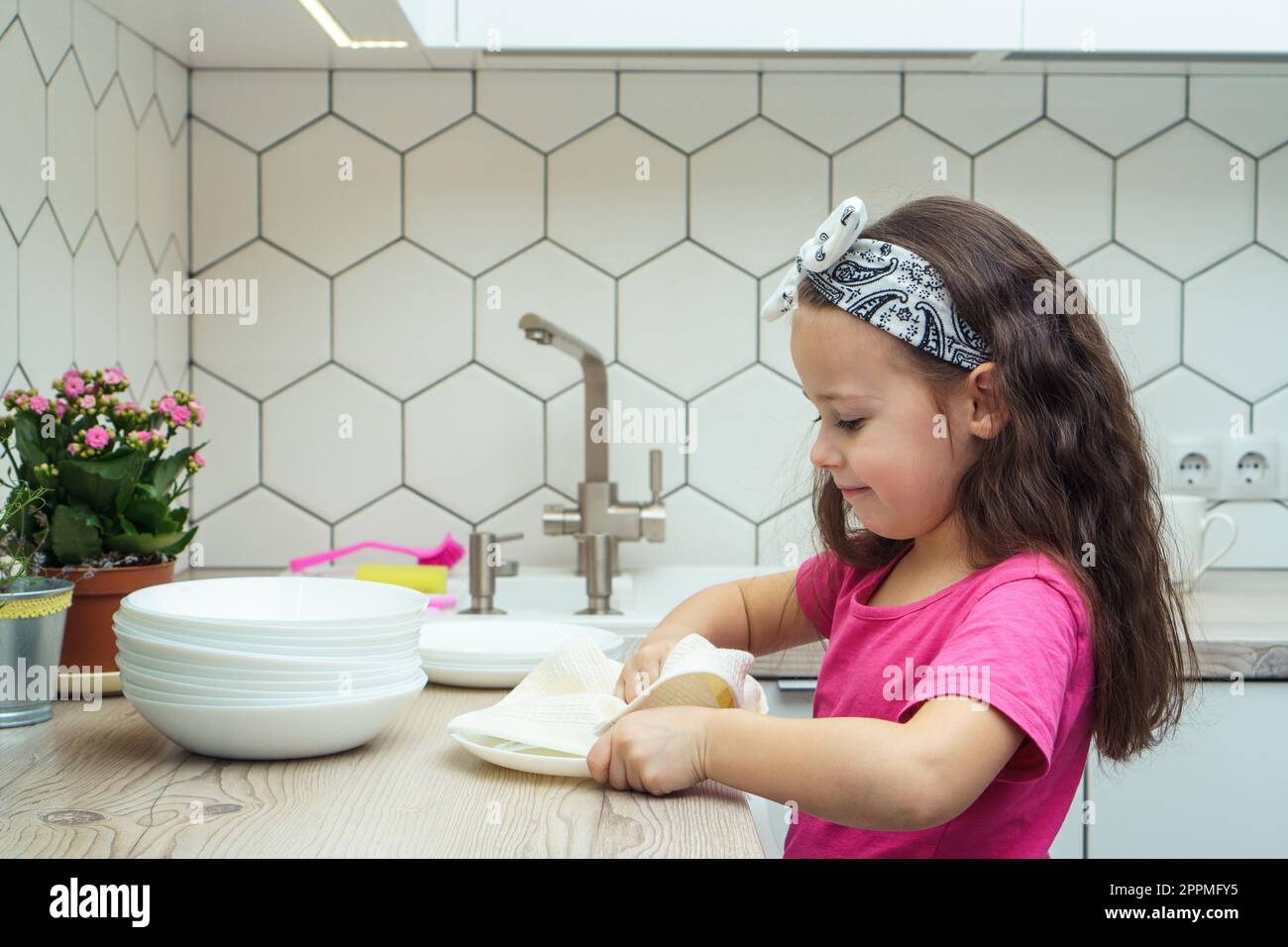 Une Enfant Caucasienne Sèche La Vaisselle Dans La Cuisine En Essuyant Avec  Un Torchon De Cuisine Les Parents Aident Le Concept Copier L'espace