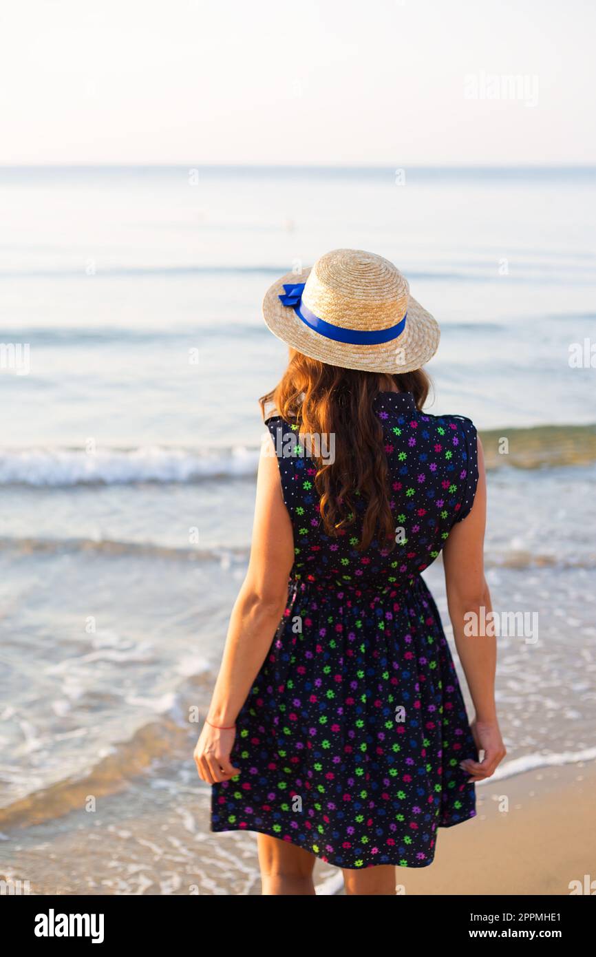 Belle jeune fille au chapeau se distingue avec son dos sur une plage de sable. Banque D'Images