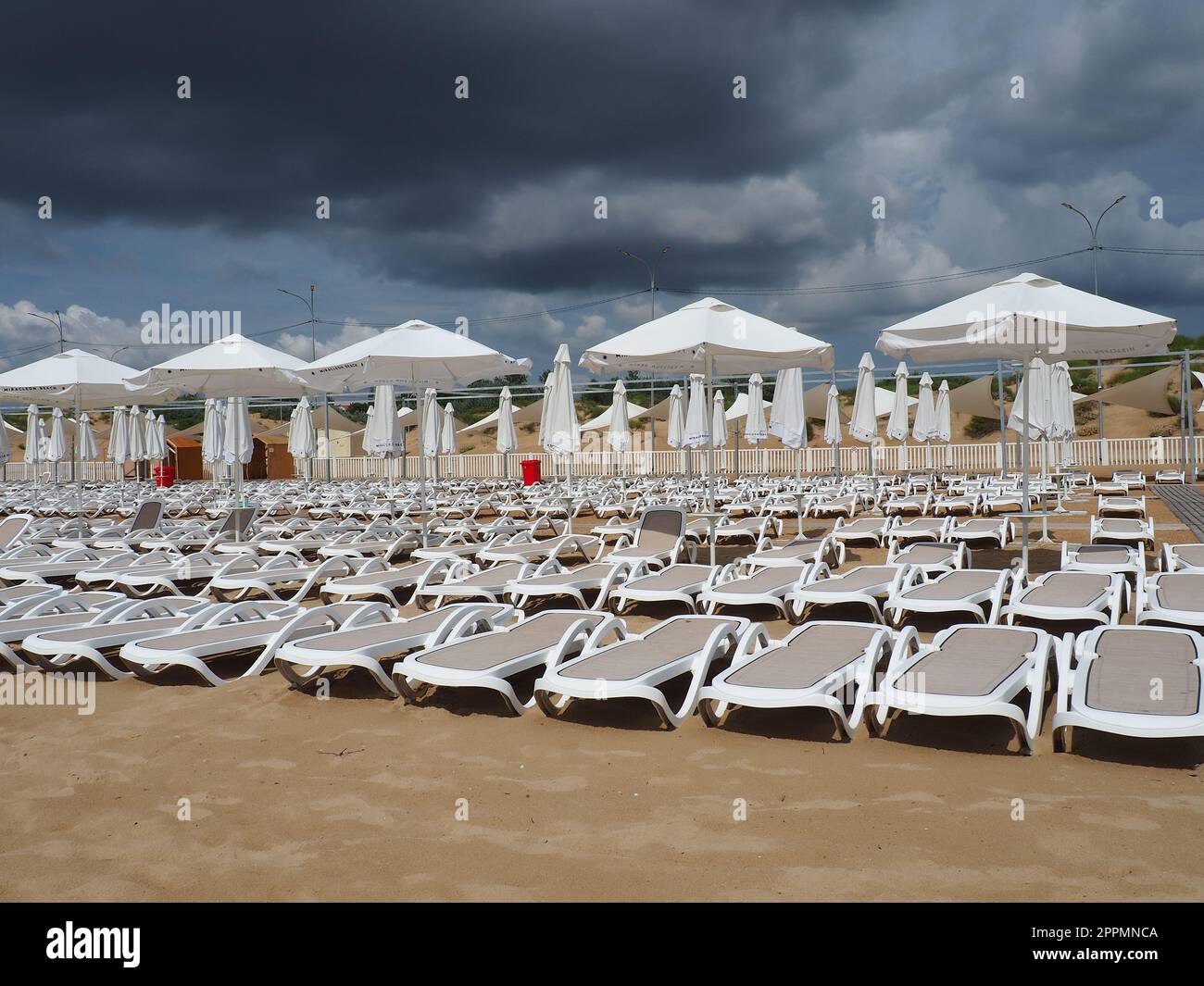 Transats humides et parasols sur la plage de la mer pendant la tempête de pluie forte. Parasol roulé sur la plage contre le ciel nuageux sombre. Invasion d'un typhon, d'un cyclone ou d'une tempête sur la mer ou l'océan. Saison de plage. Banque D'Images