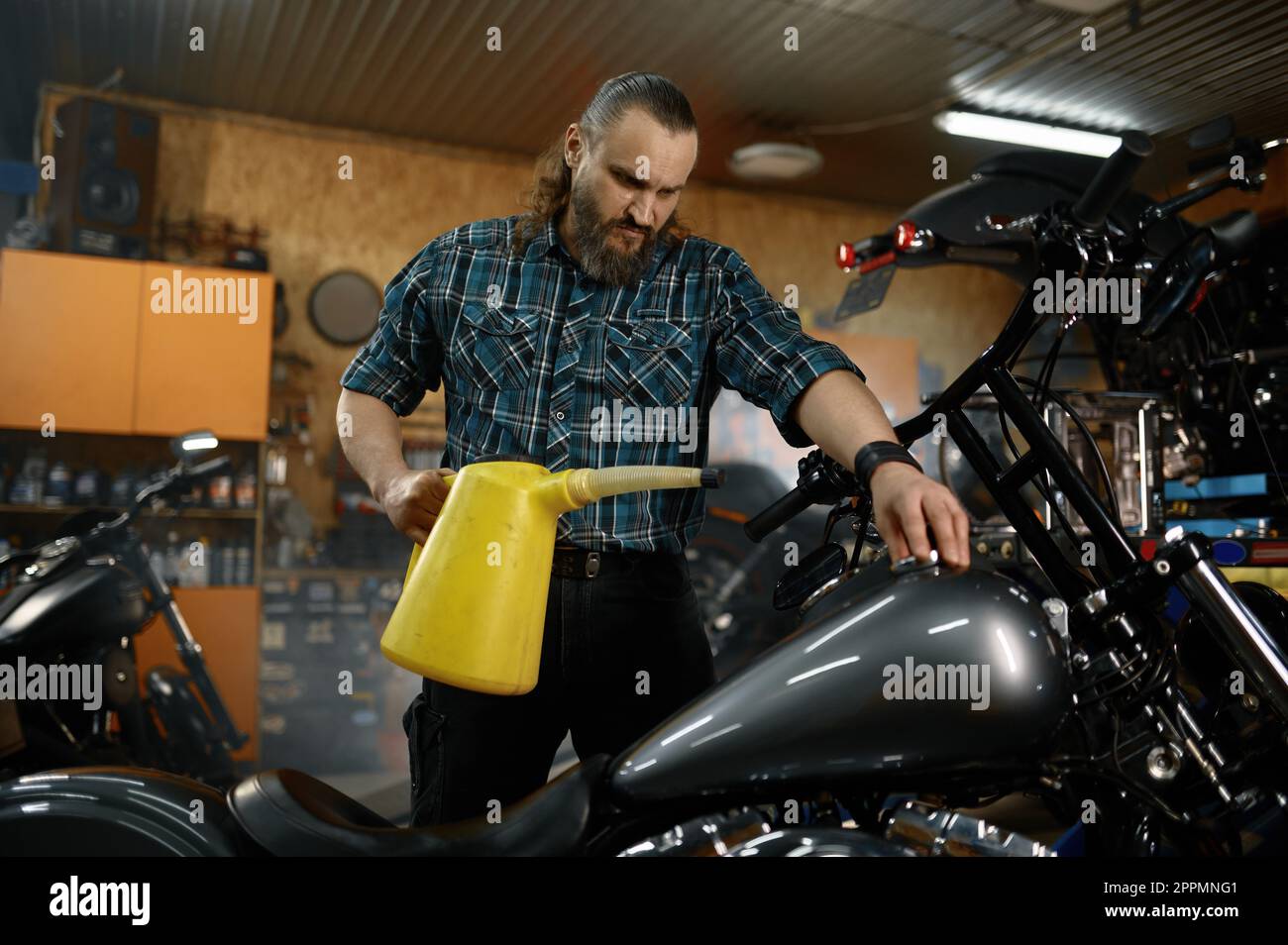 Homme motard ravitaillant la moto dans le garage après les travaux de réparation Banque D'Images