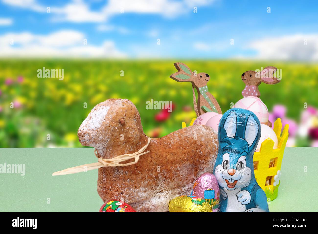 Carte de Pâques. Un gâteau d'agneau traditionnel de Pâques, un lapin de pâques, des bonbons au chocolat et un panier avec des œufs et des lapins en bois sur fond printanier flou abstrait. Banque D'Images