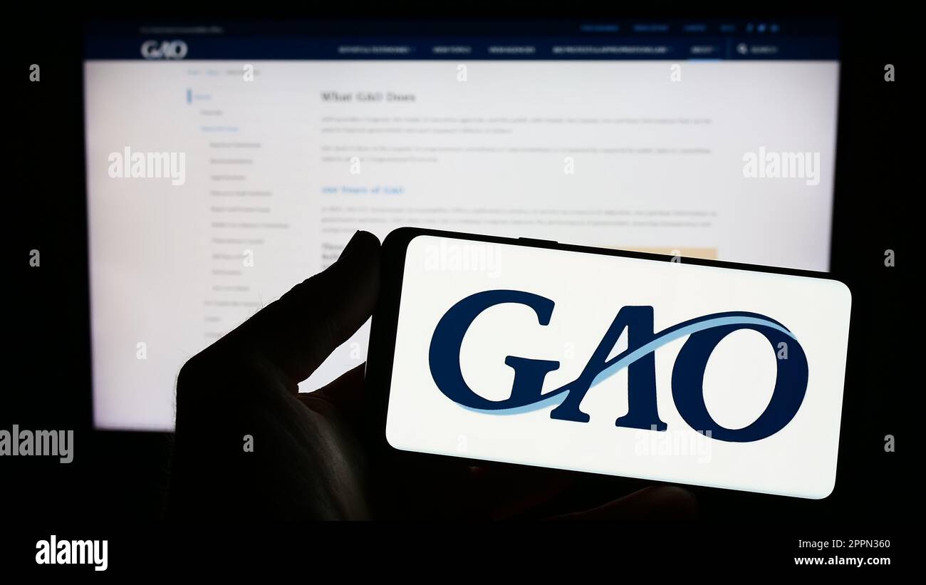 Personne tenant un smartphone avec le logo de l'Office de responsabilité du gouvernement des États-Unis (GAO) à l'écran devant le site Web. Mise au point sur l'affichage du téléphone. Banque D'Images
