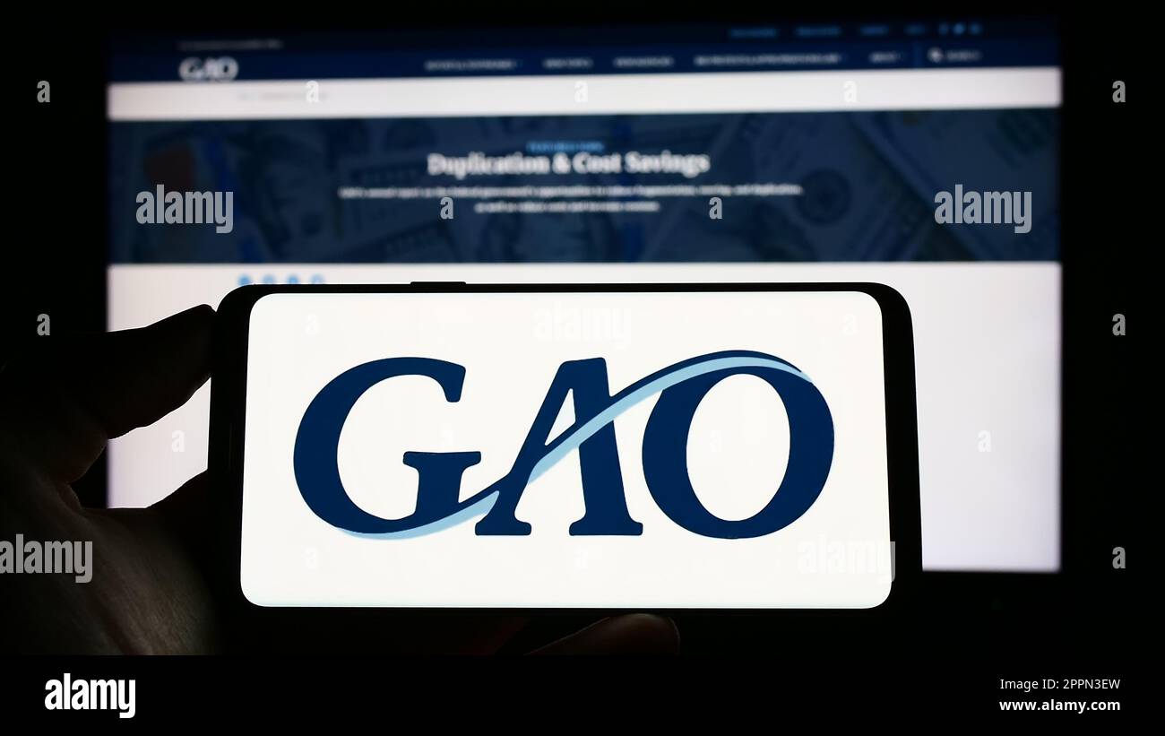 Personne tenant un téléphone portable avec le logo de l'Office de responsabilité du gouvernement des États-Unis (GAO) à l'écran devant la page Web. Mise au point sur l'affichage du téléphone. Banque D'Images