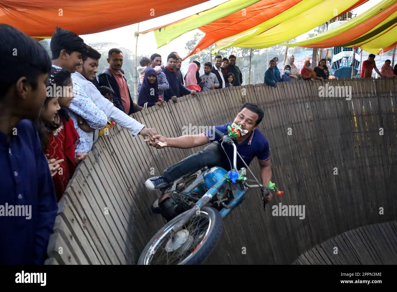 Manikgonj, Manikgonj, Bangladesh. 24th avril 2023. Un homme conduisant une moto a atteint pour de l'argent tout en réalisant des cascades en conduisant des motos sur un « mur de la mort » vertical à Manikgonj, Bangladesh. Les artistes voyagent sans équipement de protection à des vitesses allant jusqu'à 80 km/h afin que leur véhicule puisse s'équilibrer sur la planche en bois de 25 pieds de haut. Crédit : ZUMA Press, Inc./Alay Live News Banque D'Images
