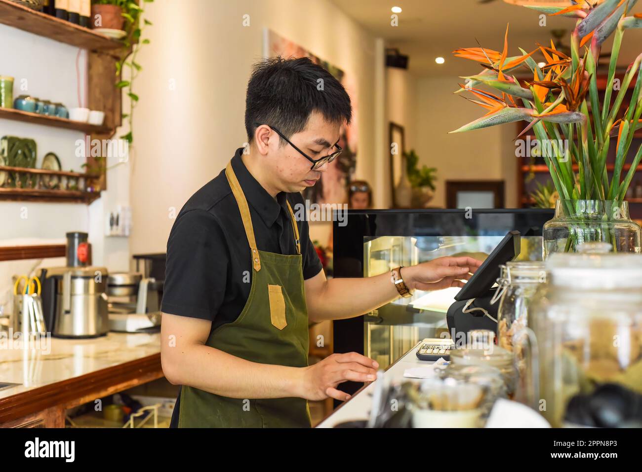 Un serveur vietnamien travaillant au comptoir avec une machine à caisses dans un café Banque D'Images