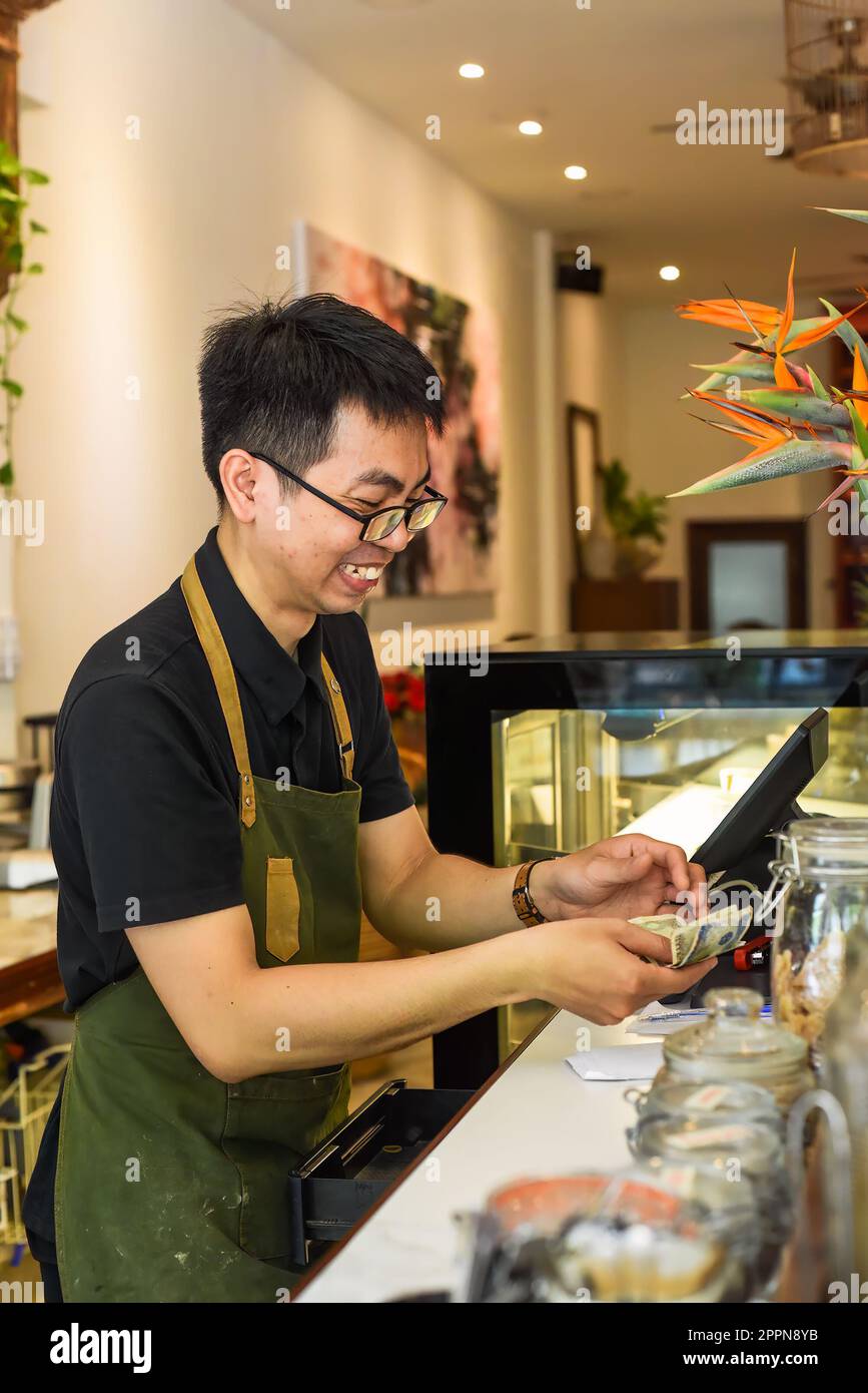 Un serveur vietnamien travaillant au comptoir avec une machine à caisses dans un café Banque D'Images