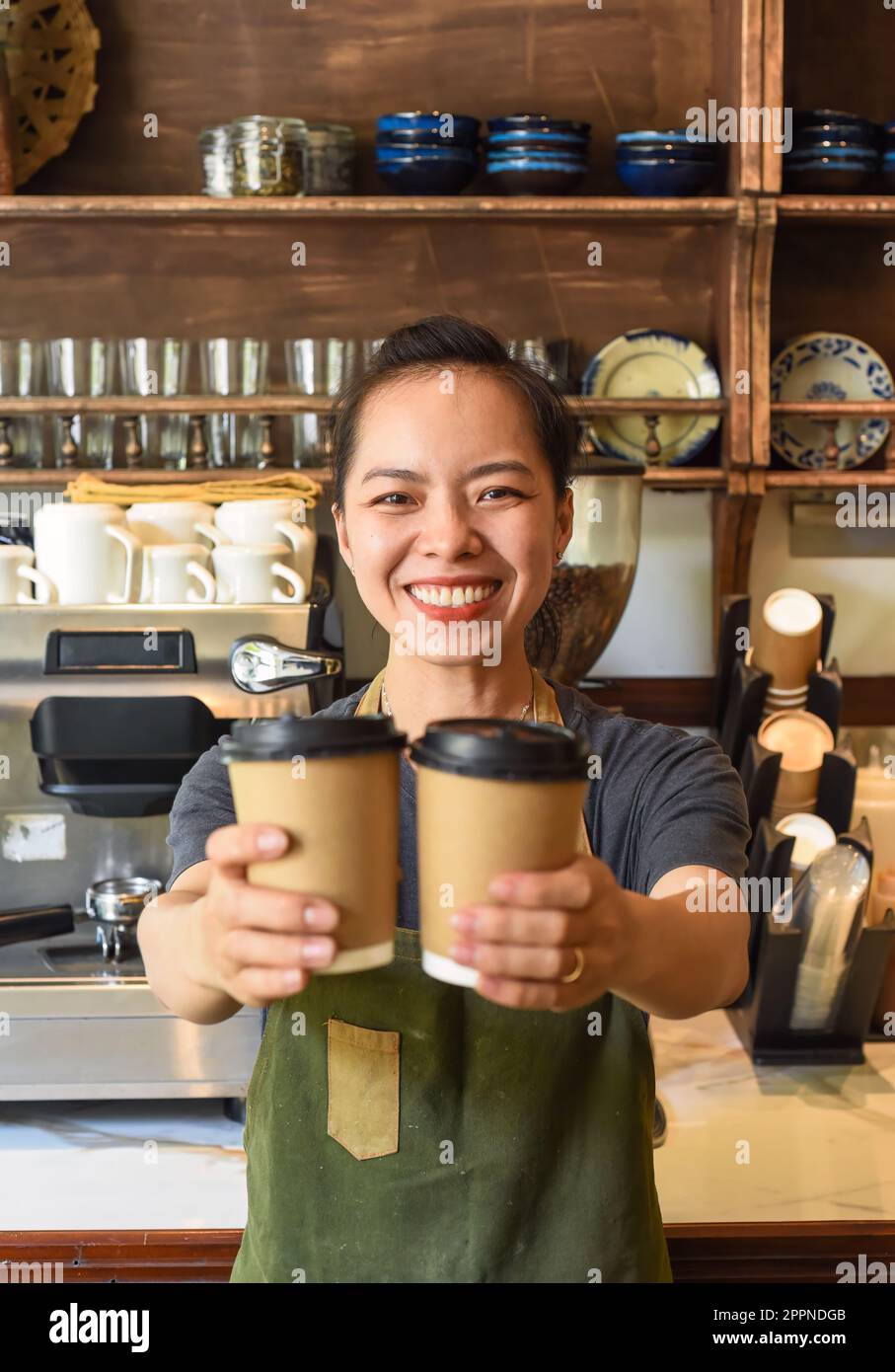 Une serveuse vietnamienne souriante tenant des tasses en papier avec du café dans un café Banque D'Images