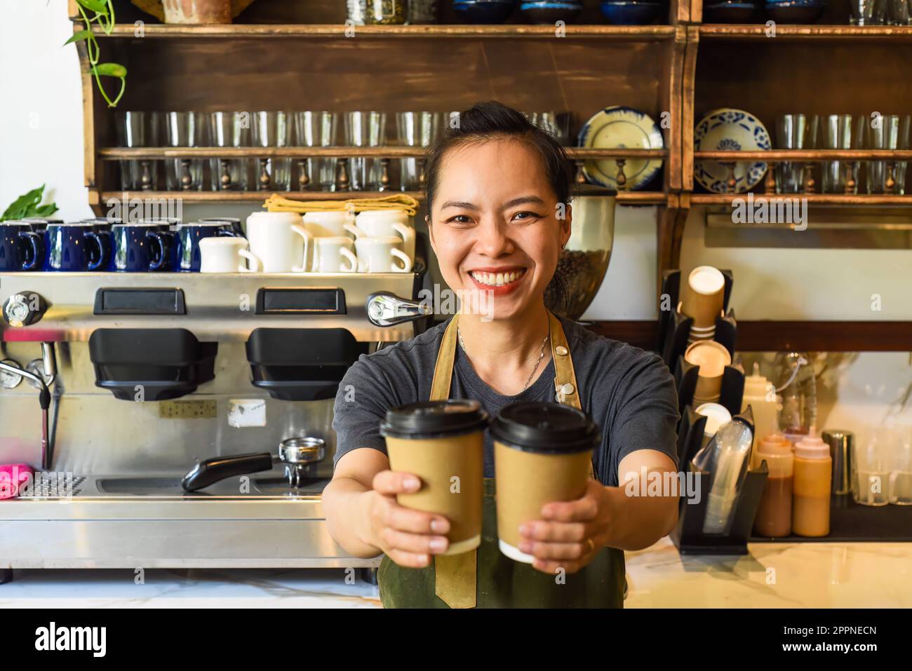 Une serveuse vietnamienne souriante tenant des tasses en papier avec du café dans un café Banque D'Images