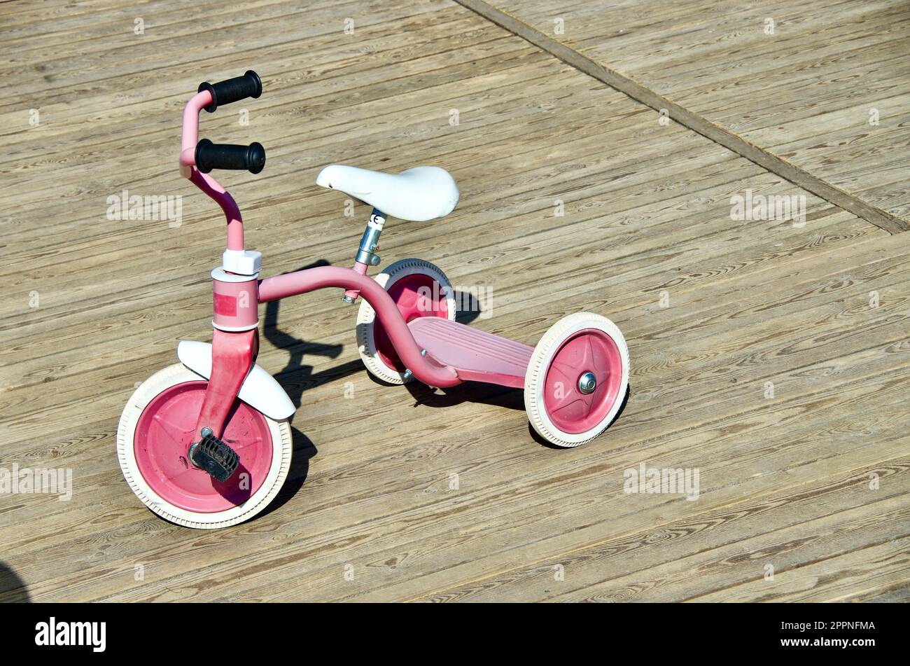 Tricycle rose pour les petits enfants pour jouer et transporter à l'extérieur sur une aire de jeux en bois. Banque D'Images