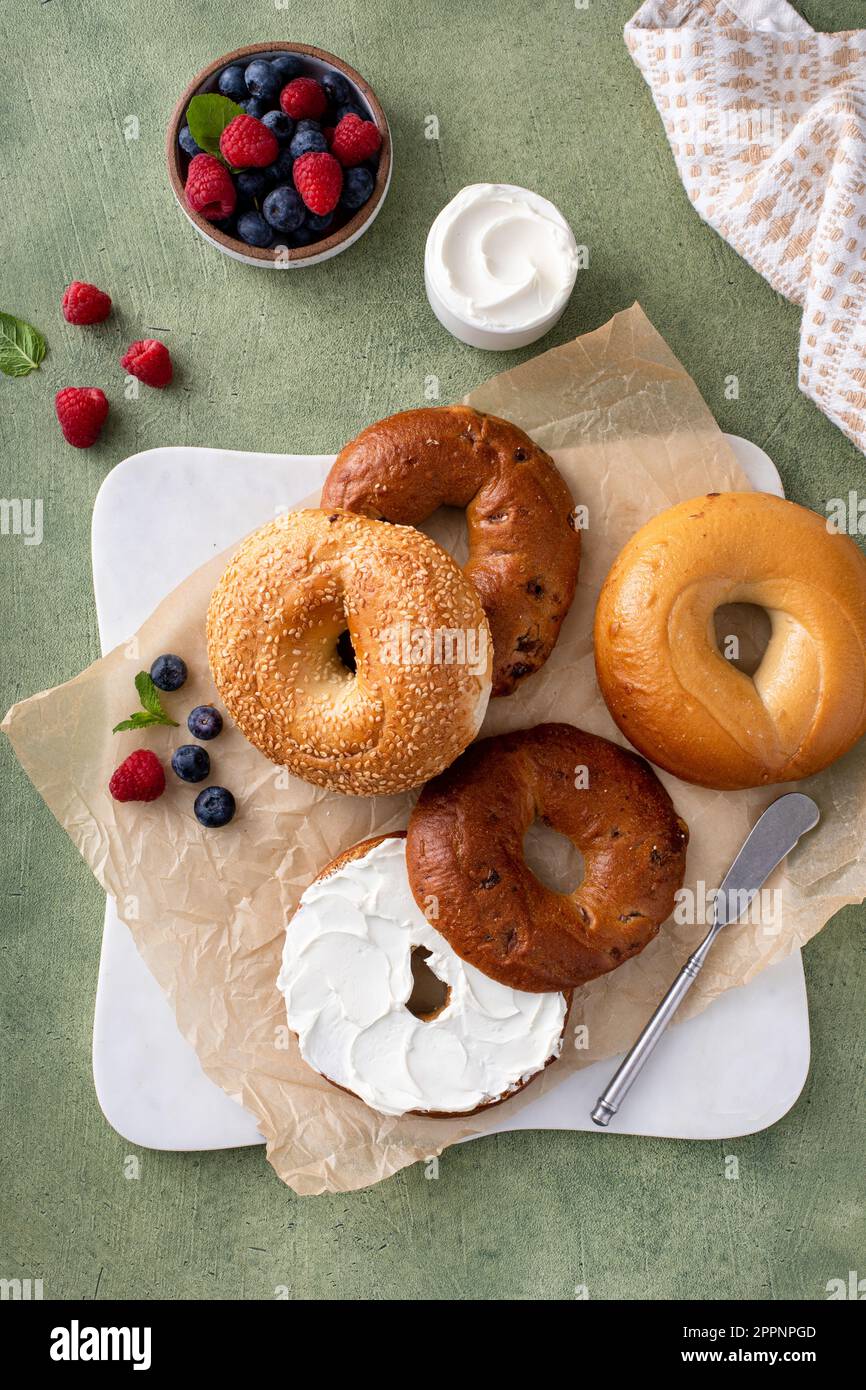 Bagels maison fraîchement cuits sur un papier parchemin prêt à manger, raisins secs de cannelle, sésame et bagel simple servi avec du fromage à la crème et des baies fraîches Banque D'Images