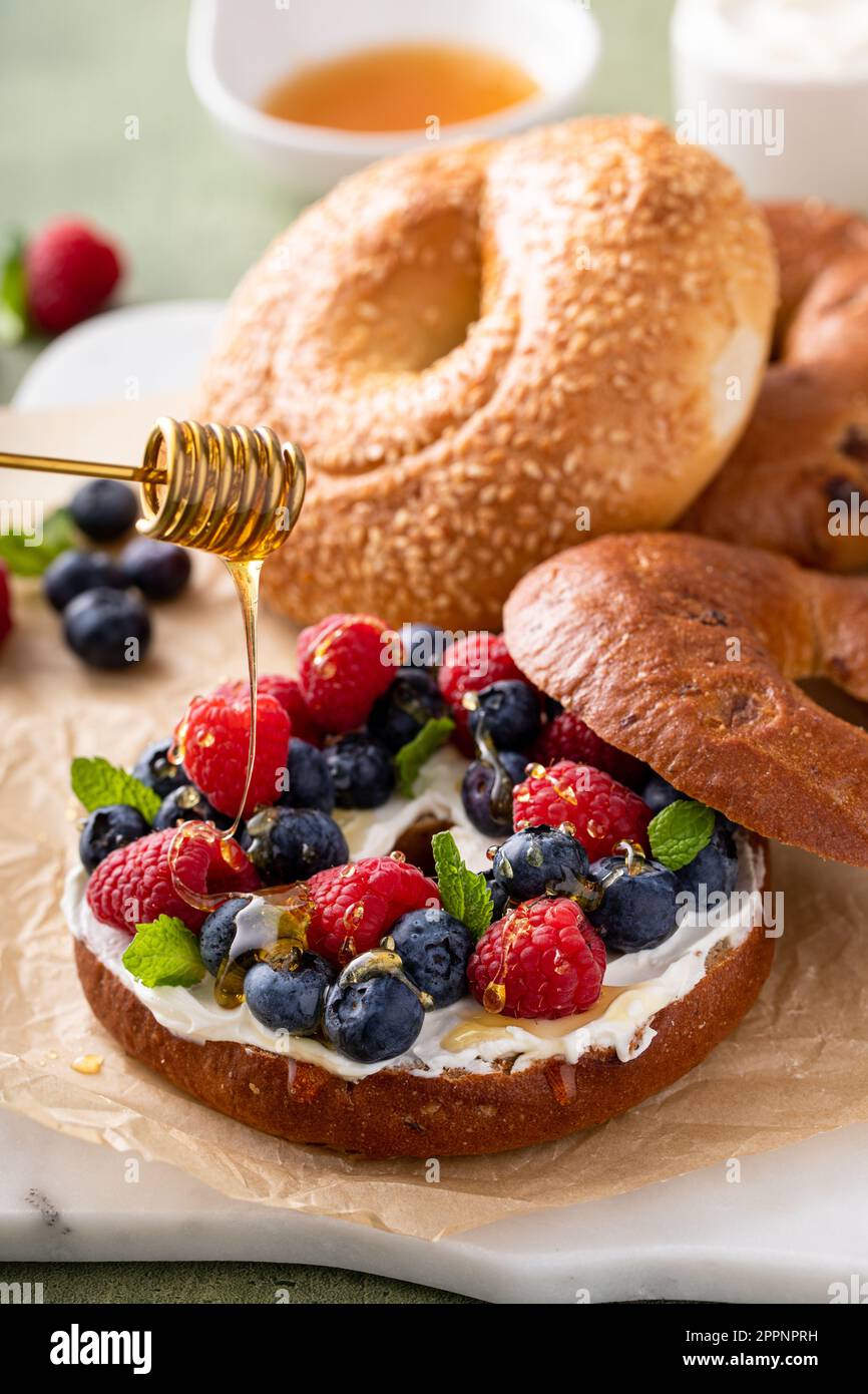 Bagels maison fraîchement cuits sur un papier parchemin prêt à manger, bagel de raisins secs à la cannelle avec fromage à la crème et baies fraîches arrosées de miel Banque D'Images