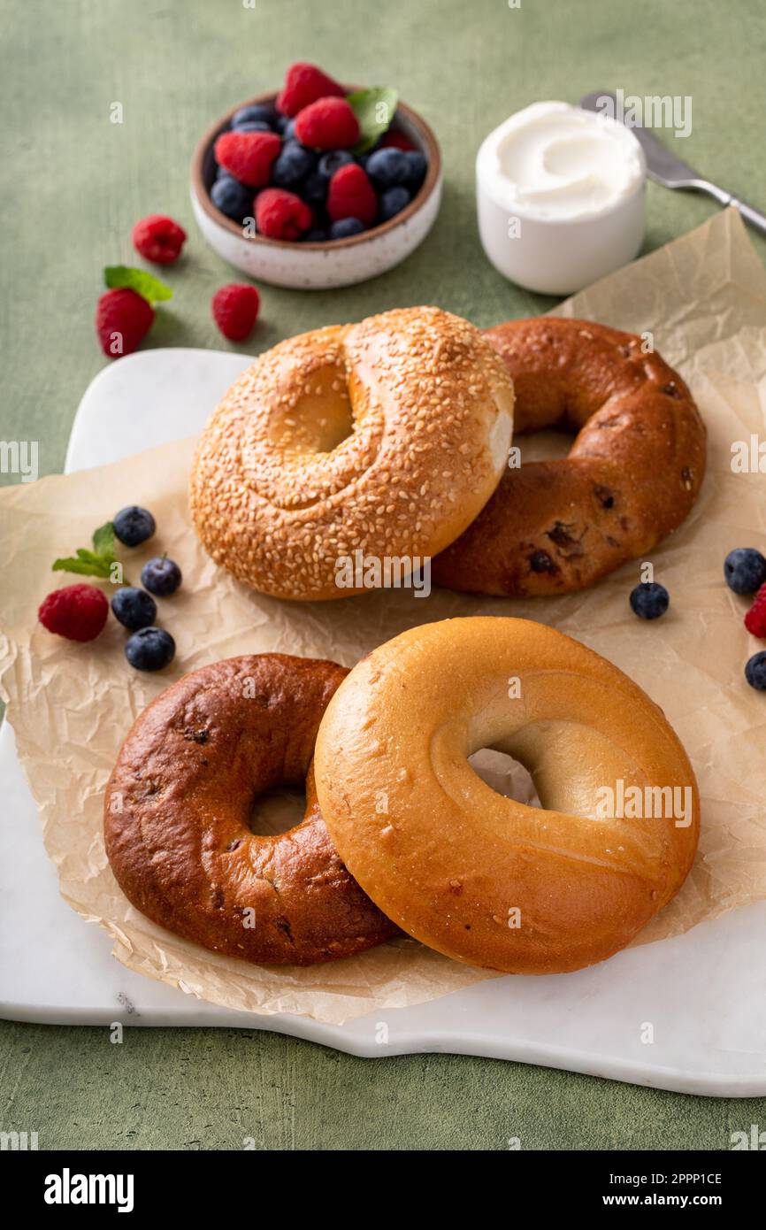 Bagels maison fraîchement cuits sur un papier parchemin prêt à manger, raisins secs de cannelle, sésame et bagel simple servi avec du fromage à la crème et des baies fraîches Banque D'Images