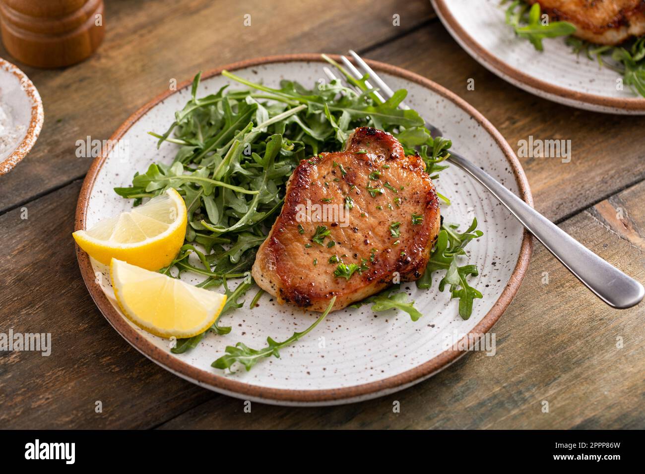 Côtelettes de porc cuites à l'ail servies avec une salade d'arugula sur une assiette Banque D'Images