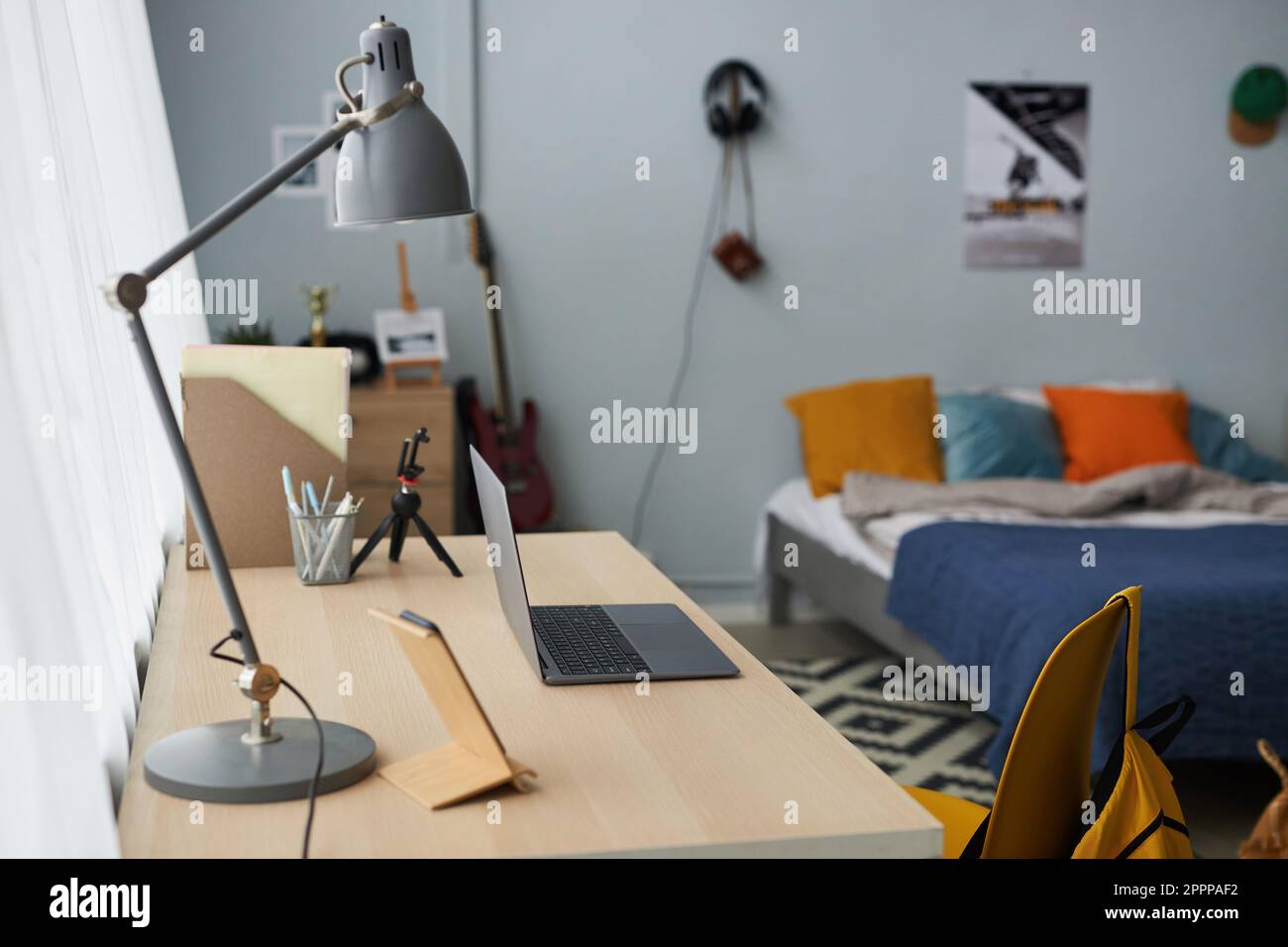 Lieu de travail de l'adolescent étudiant avec lampe, ordinateur portable, image, trépied pour smartphone et crayons dans un petit bac contre lit double avec coussins Banque D'Images