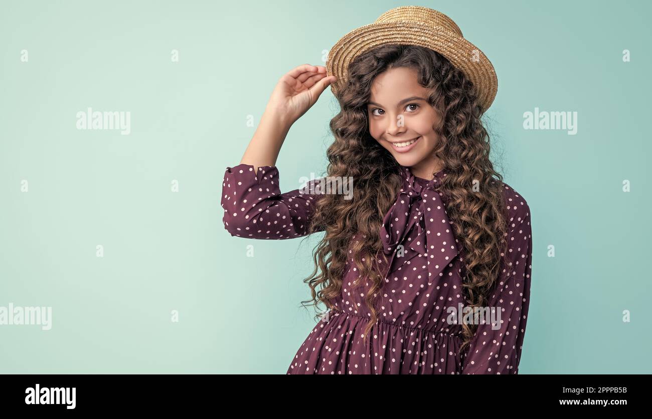 enfant souriant en chapeau de paille avec de longs cheveux bruns sur fond bleu Banque D'Images