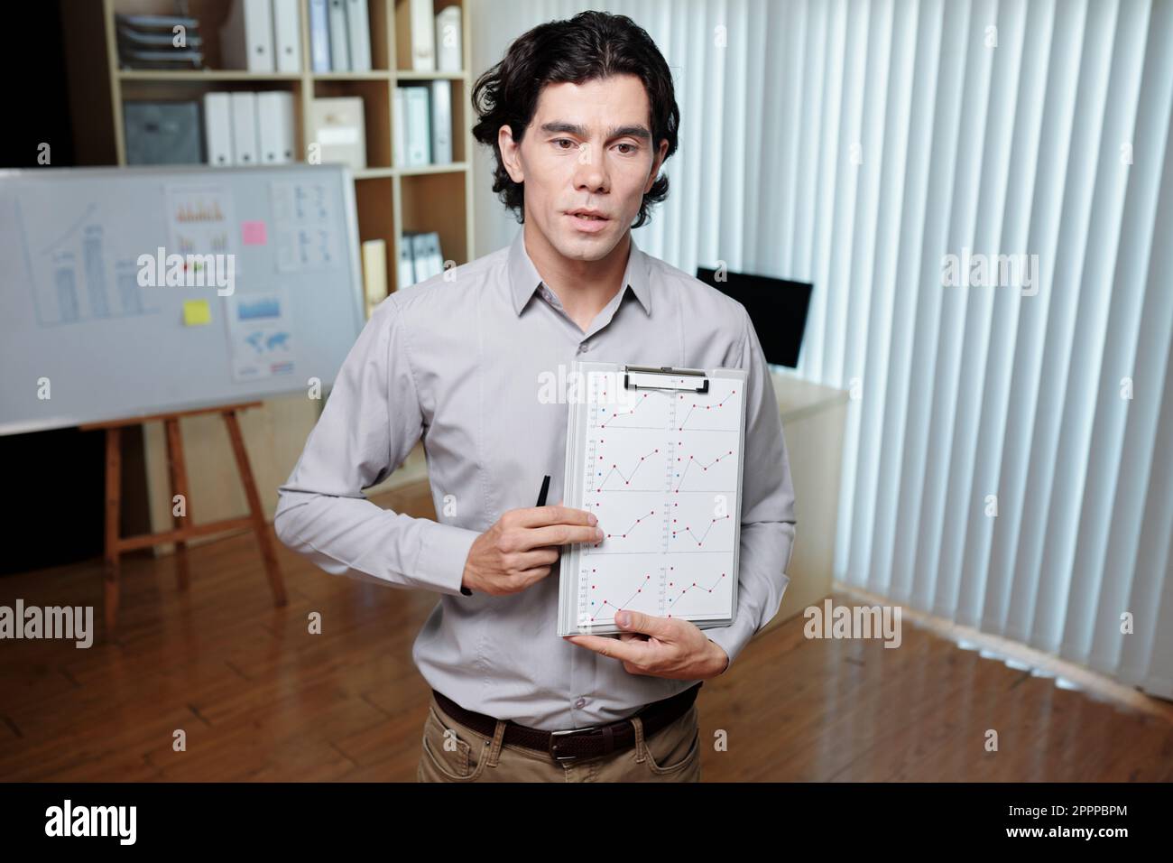 Jeune homme d'affaires confiant en vêtements décontractés intelligents montrant un document financier avec des graphiques et expliquant les données au public Banque D'Images