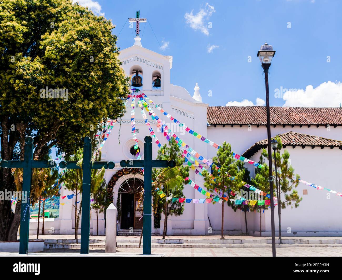 L'église emblématique de San Lorenzo avec des drapeaux de prière colorés et trois croix chrétiennes dans son parvis , Zinacantan, Chiapas, Mexique Banque D'Images