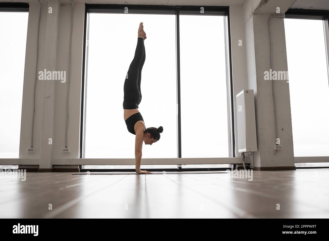 Femme yogi faisant appui sur la tête de lit tout en pratiquant le yoga dans un studio lumineux spécial. Jeune femme en leggings noirs et brassière avec matelas de sport pour l'entraînement. Concept de soins de l'esprit et du corps. Banque D'Images