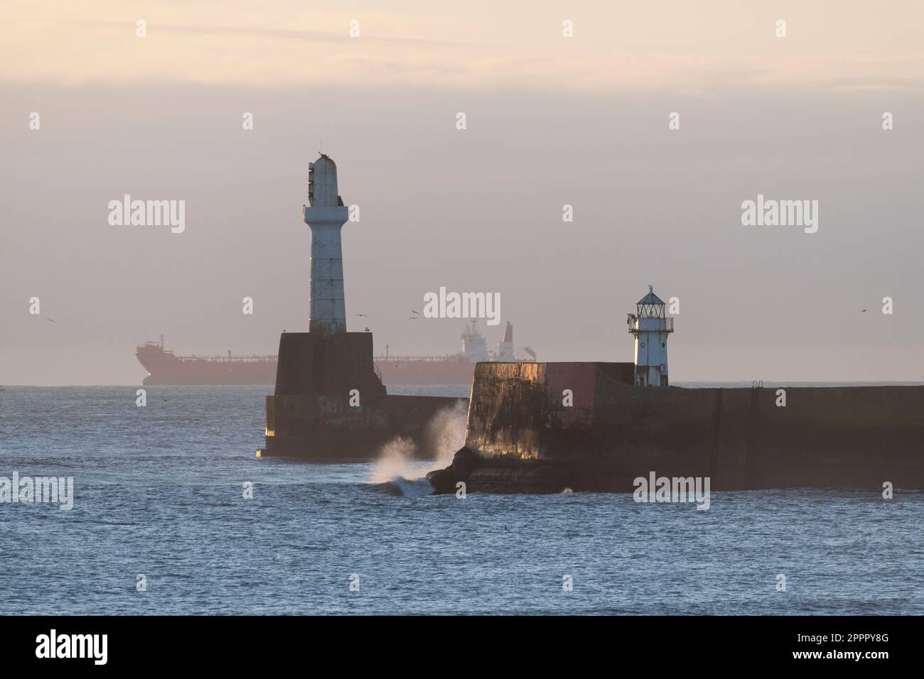 Le phare de South Breakwater et North Pier s'allume à l'entrée du port d'Aberdeen en début de matinée avec un pétrolier à l'horizon Banque D'Images