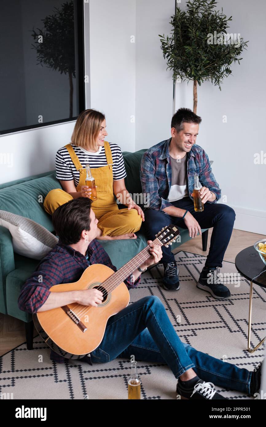 Trois jeunes hommes jouant de la guitare tout en ayant quelques bières dans leur salon et en ayant un après-midi amusant. Concept: Style de vie, jouer de la guitare, r Banque D'Images