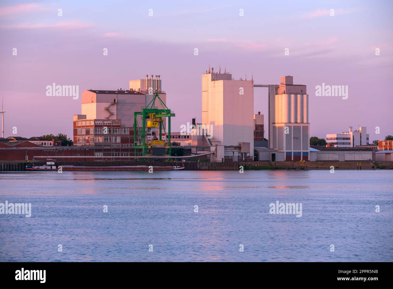 Quai commercial avec une grue à portique, des silos et un entrepôt dans un port fluvial au coucher du soleil en été Banque D'Images