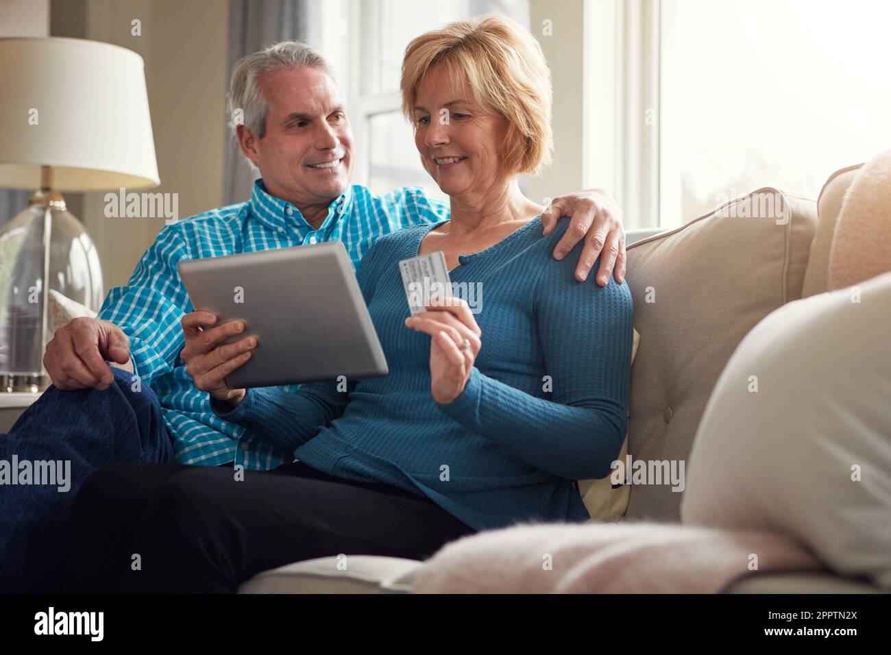 Évitez les foules, faites du shopping dans le confort. un heureux couple mature se relaxant sur le canapé et utilisant une tablette numérique et une carte de crédit ensemble. Banque D'Images