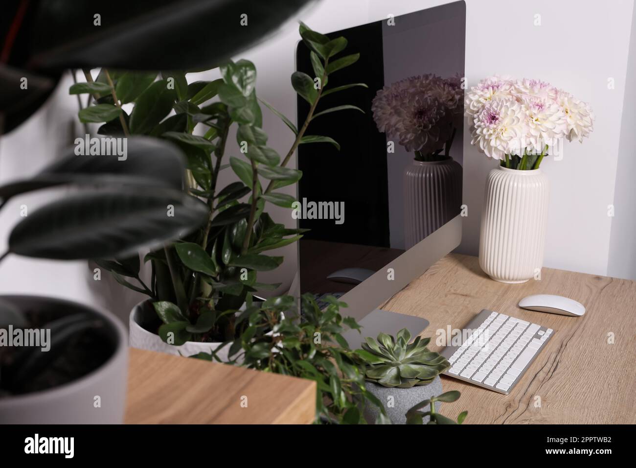 Espace de travail confortable avec ordinateur moderne, plantes vertes et belles fleurs sur table en bois à l'intérieur Banque D'Images