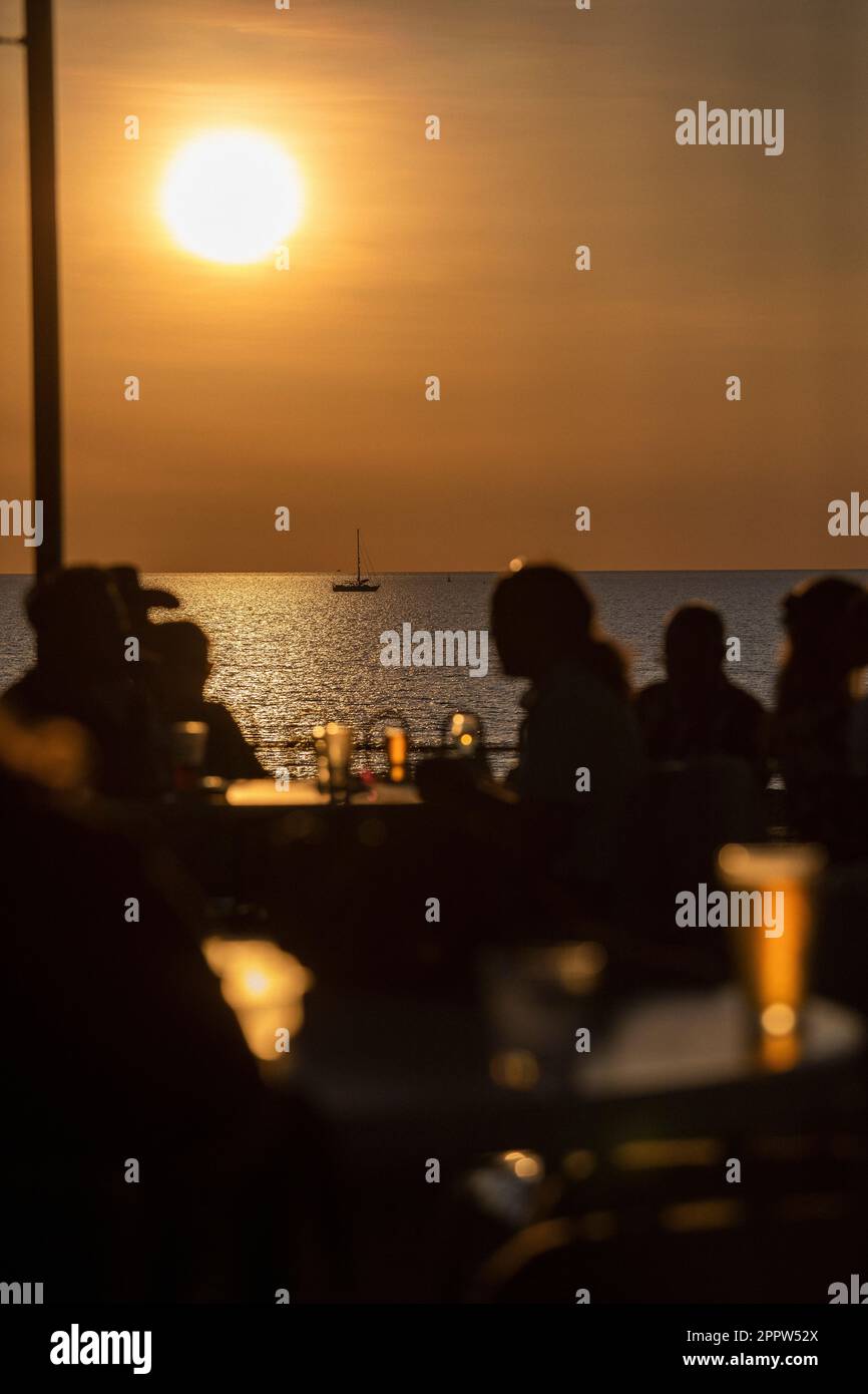 Des gens silhouetés boivent de la bière sur le patio en bord de mer avec vue sur l'océan au coucher du soleil Banque D'Images