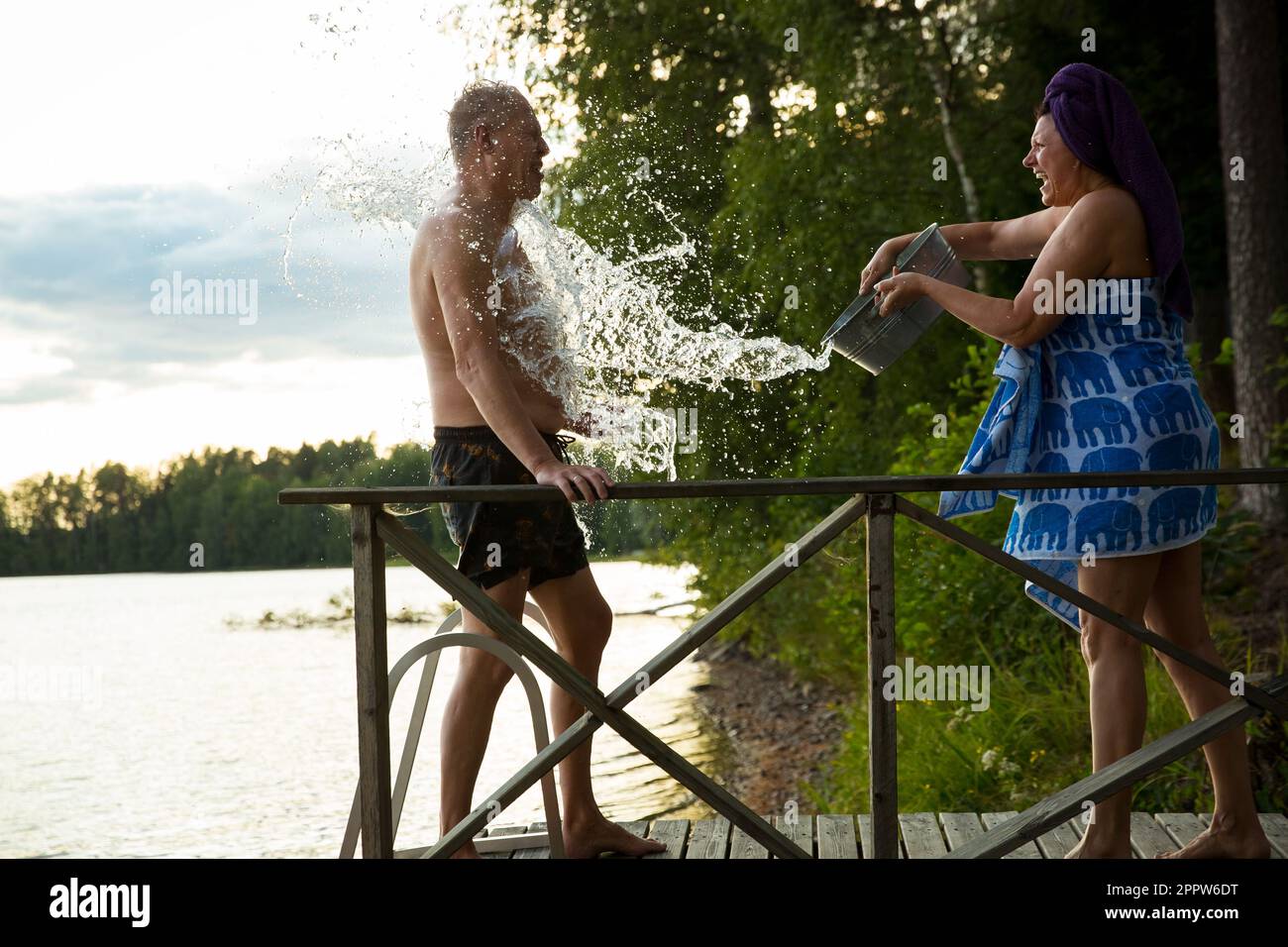 Un couple âgé s'est amusé après le sauna finlandais sur une jetée en bois dans un lac. Femme mature versant de l'eau froide du bassin sur son partenaire. Finlande Banque D'Images
