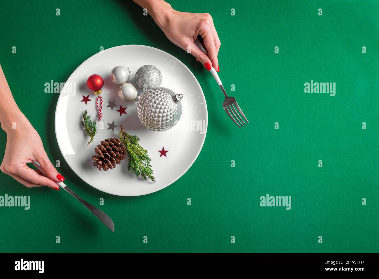 Mise en place créative de la table de Noël et mains féminines. Boules argentées festives et cône de pin sur plaque blanche sur fond vert, pose à plat, espace de copie. Manger Banque D'Images