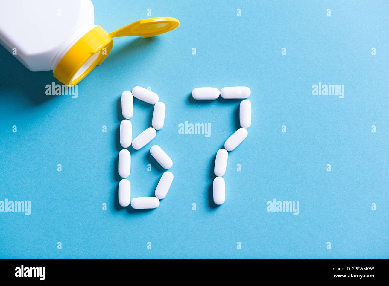 Vitamine B7, supplément de biotine. Pilules blanches formant la forme à B7 signe sur fond bleu, espace de copie, vue de dessus. Banque D'Images