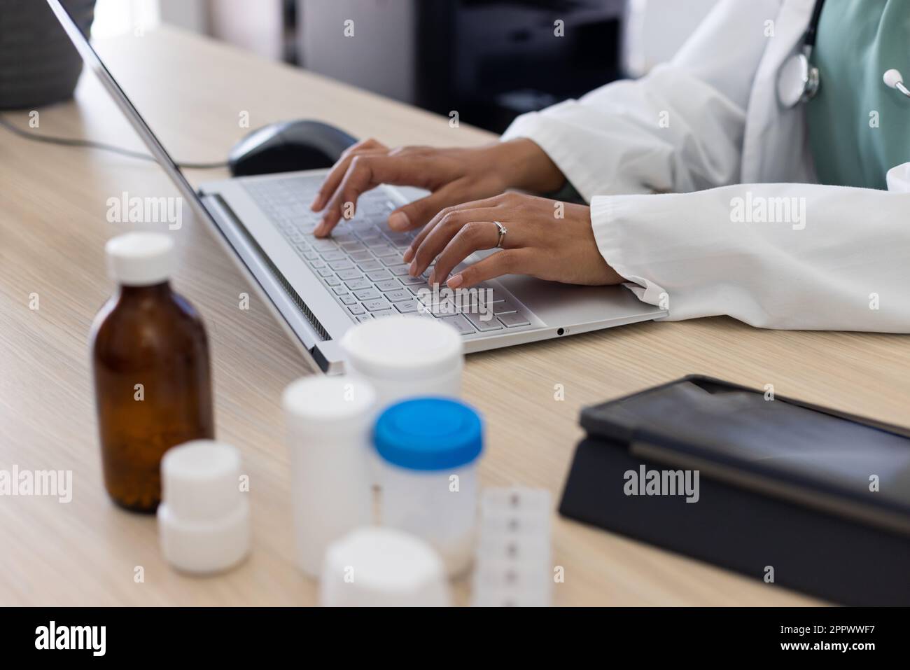 Section médiane de la femme biraciale médecin utilisant un ordinateur portable au bureau du médecin Banque D'Images