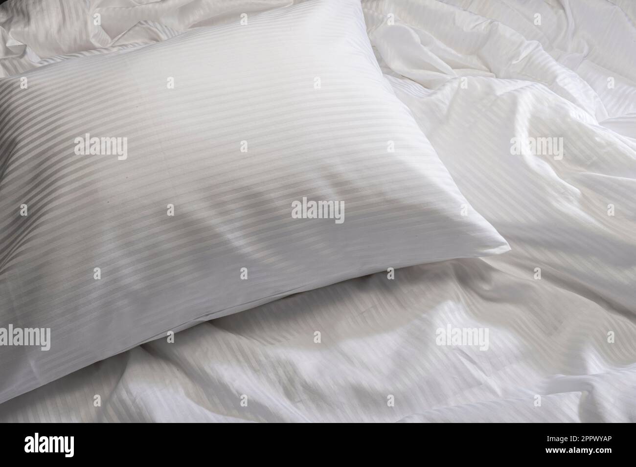 Coussin blanc sur le lit avec draps froissés Banque D'Images