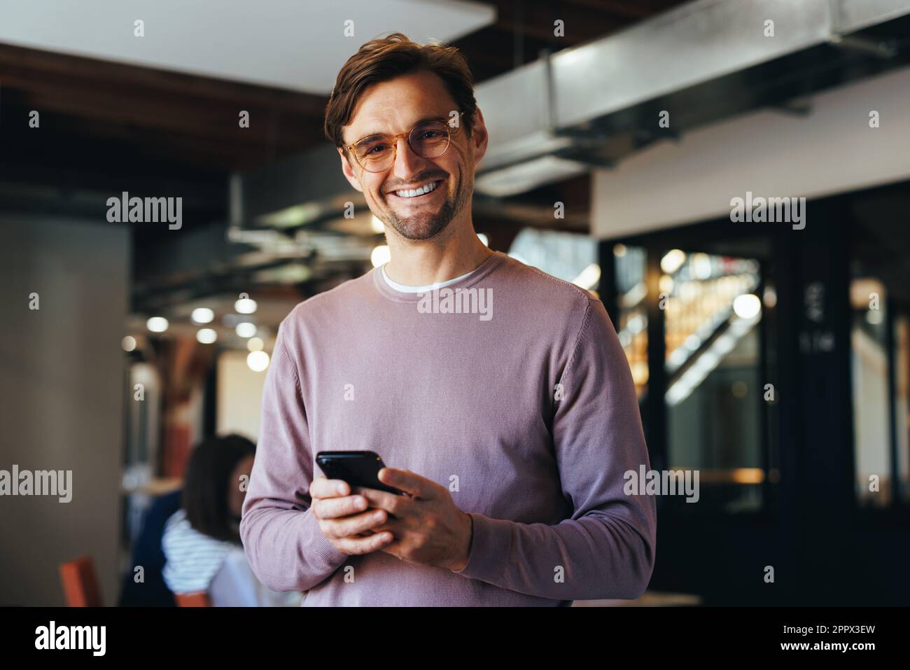 Portrait d'un homme d'affaires heureux tenant un téléphone portable dans un bureau. Homme d'affaires professionnel regardant la caméra tout en se tenant sur un lieu de travail. Banque D'Images