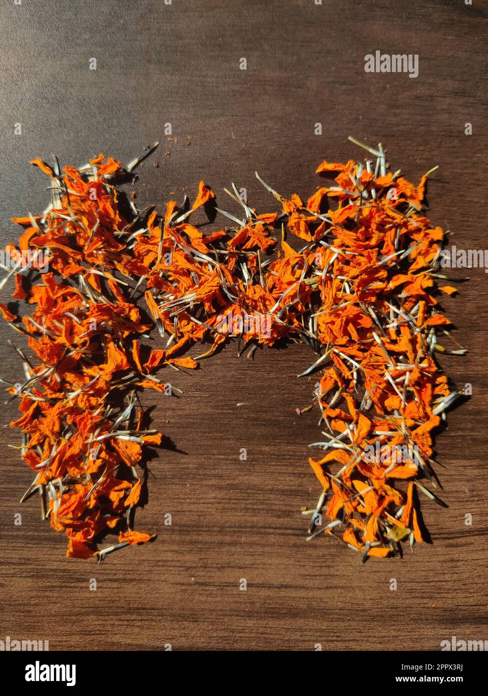 La lettre « M » est écrite avec des fleurs/graines de Marigold séchées sur une table en bois Banque D'Images