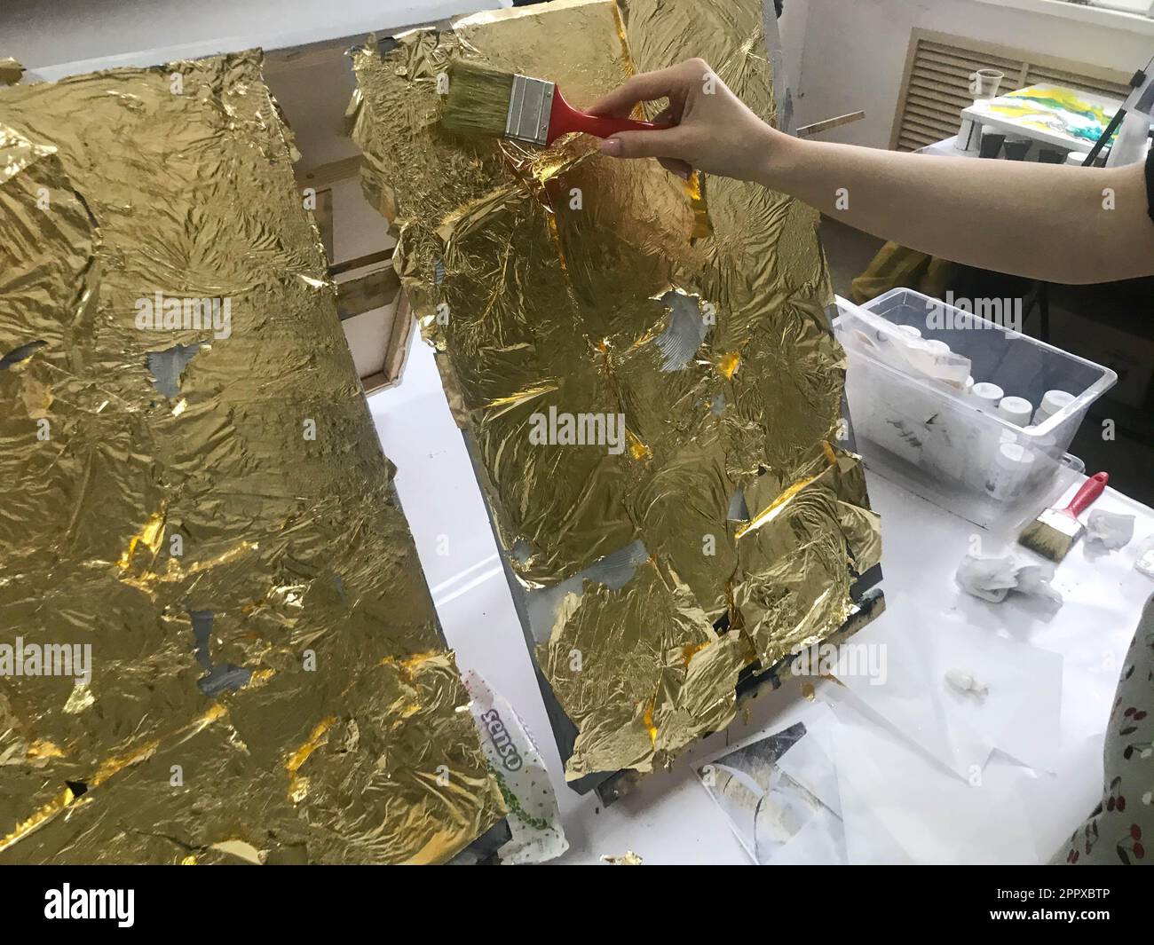 La main de l'artiste peint avec un pinceau à l'aide d'une feuille d'or jaune brillant brillant métallisé à des fins artistiques et de créativité sur toile. L'arrière Banque D'Images
