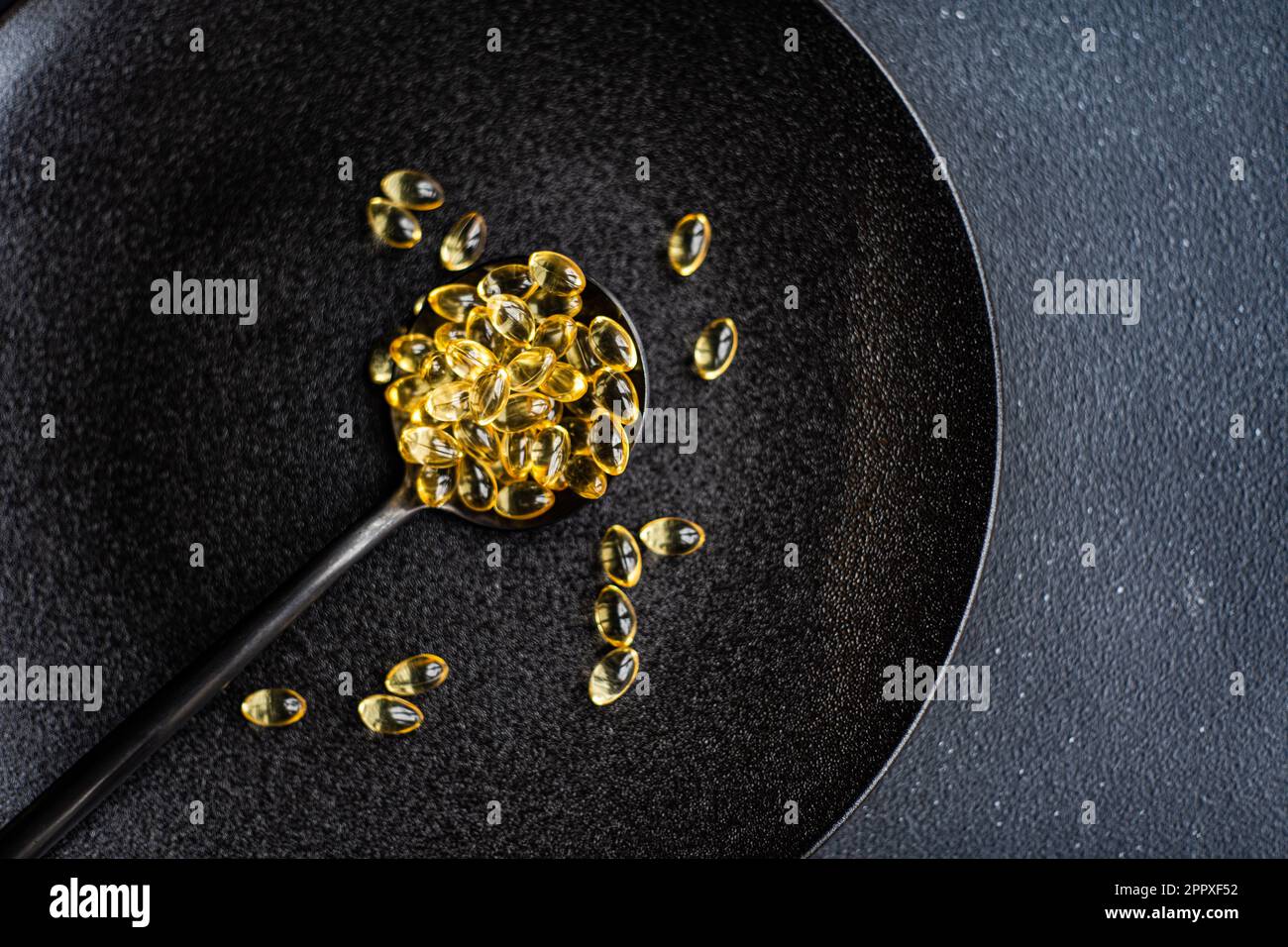 Concept de vie saine avec des médicaments de vitamine huileux dans la cuillère noire sur l'assiette de manque Banque D'Images