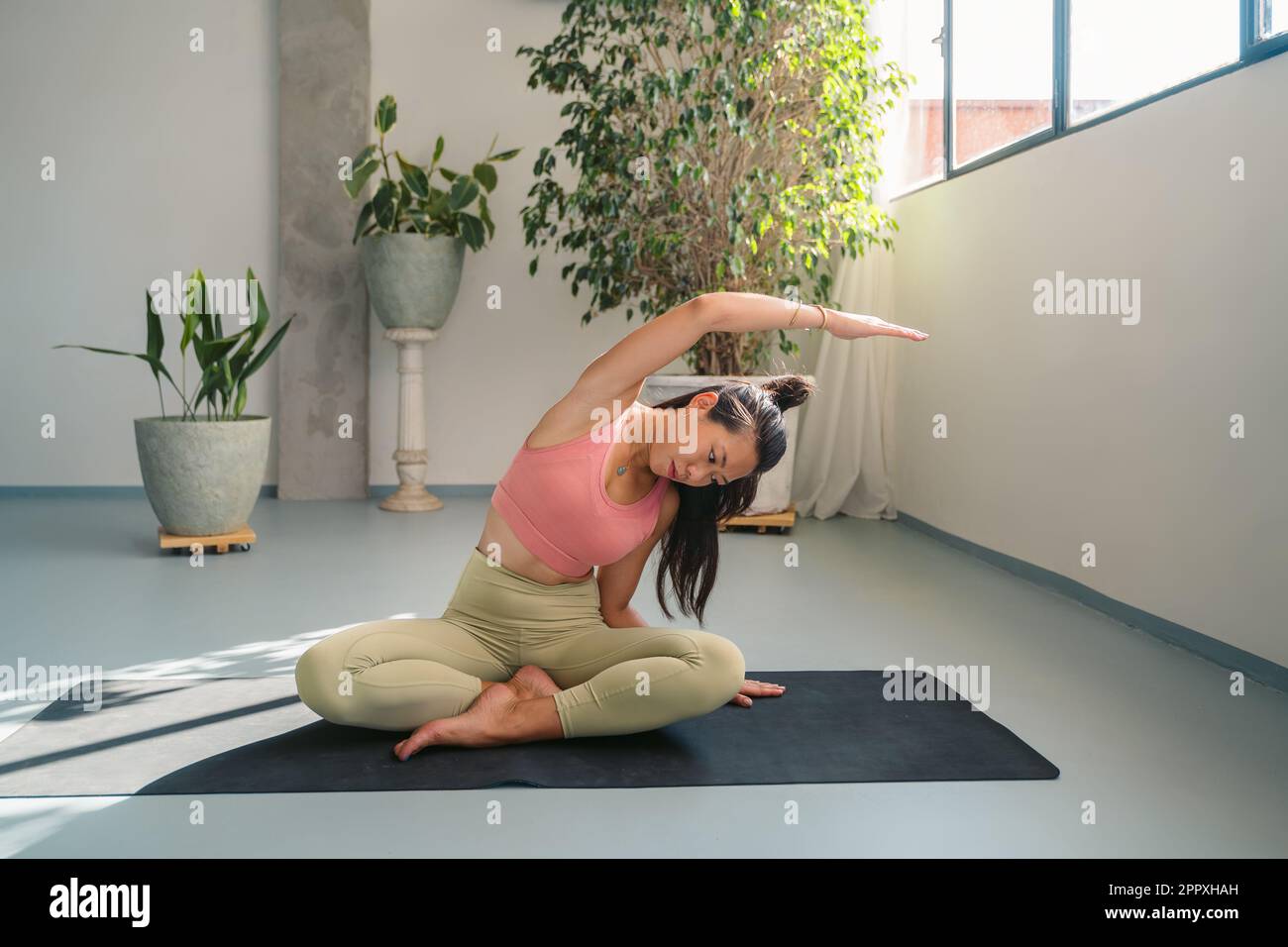 Corps complet de jeune asiatique calme et baregooted femme dans les vêtements de sport assis dans Padmasana posture tout en se pliant pendant la méditation et l'étirement du corps sur y Banque D'Images