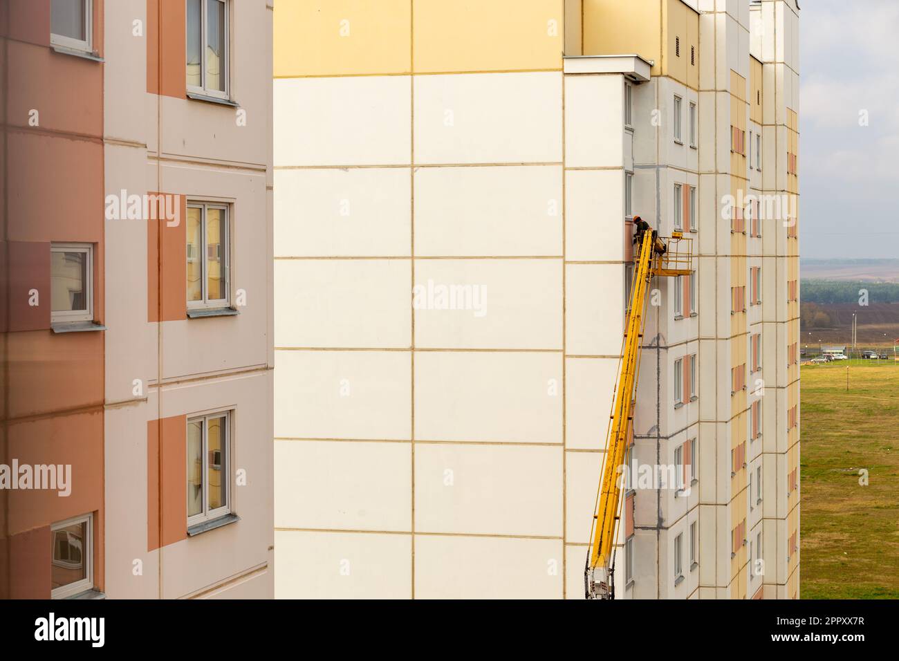 Un ouvrier dans le panier d'un ascenseur de voiture répare la façade d'un bâtiment résidentiel. Un employé de la rampe de levage hydraulique répare le balcon. Builder sur li Banque D'Images