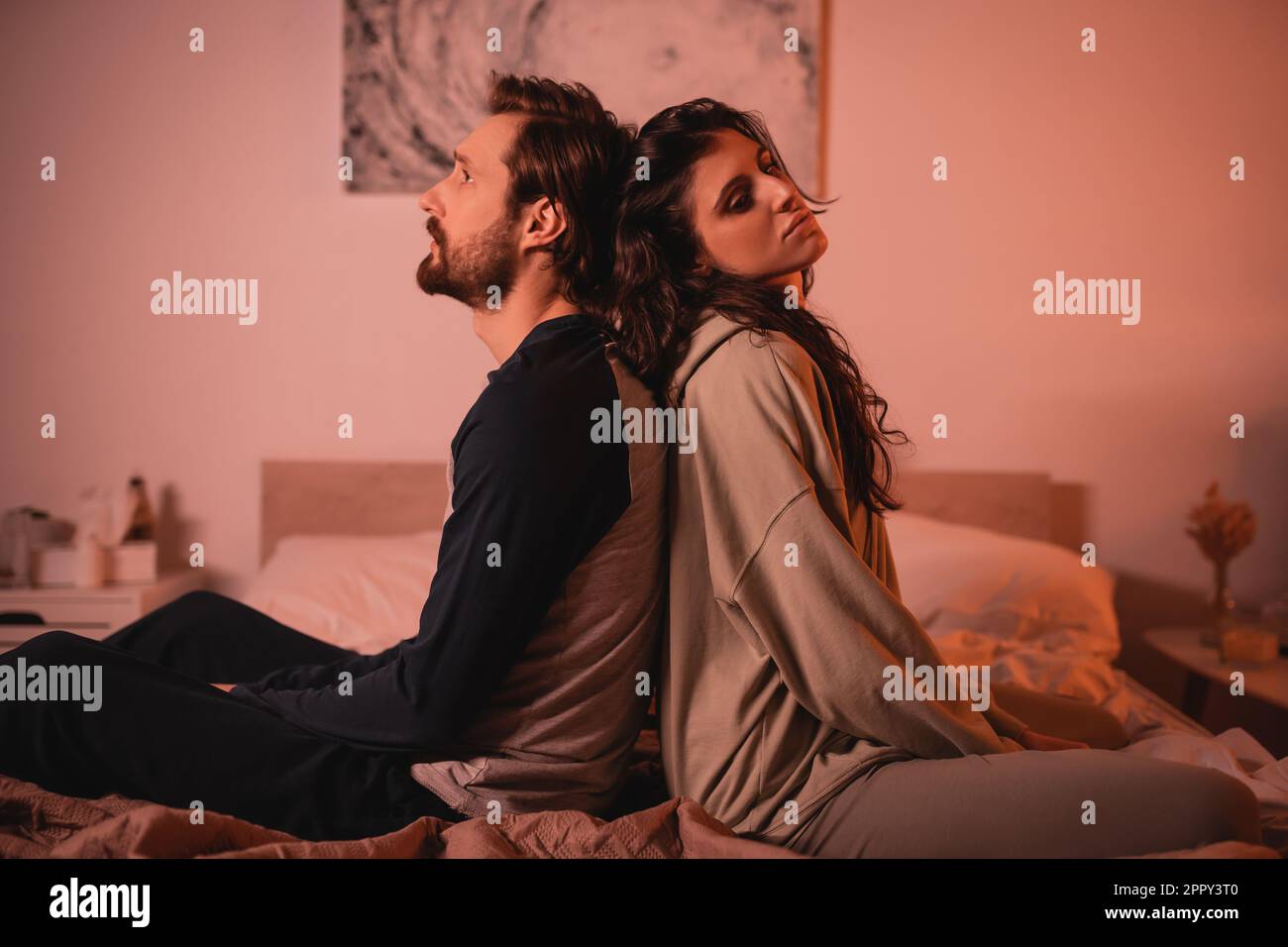 Un homme mécontent assis dos à dos avec une petite amie au lit le soir, image de stock Banque D'Images