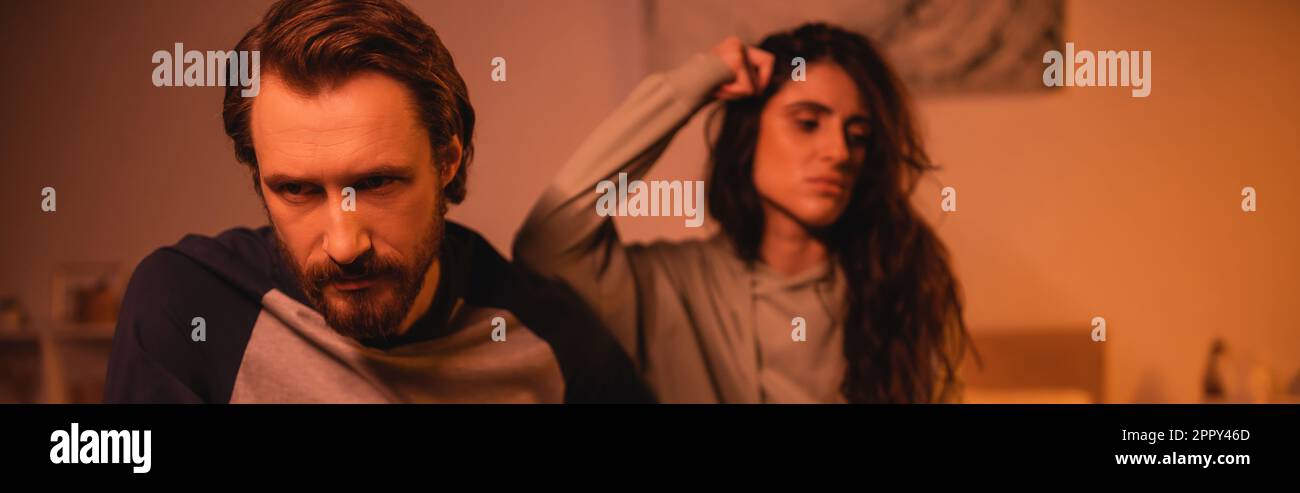 Homme insatisfait assis près d'une petite amie floue pendant la crise de relation à la maison le soir, bannière, image de stock Banque D'Images