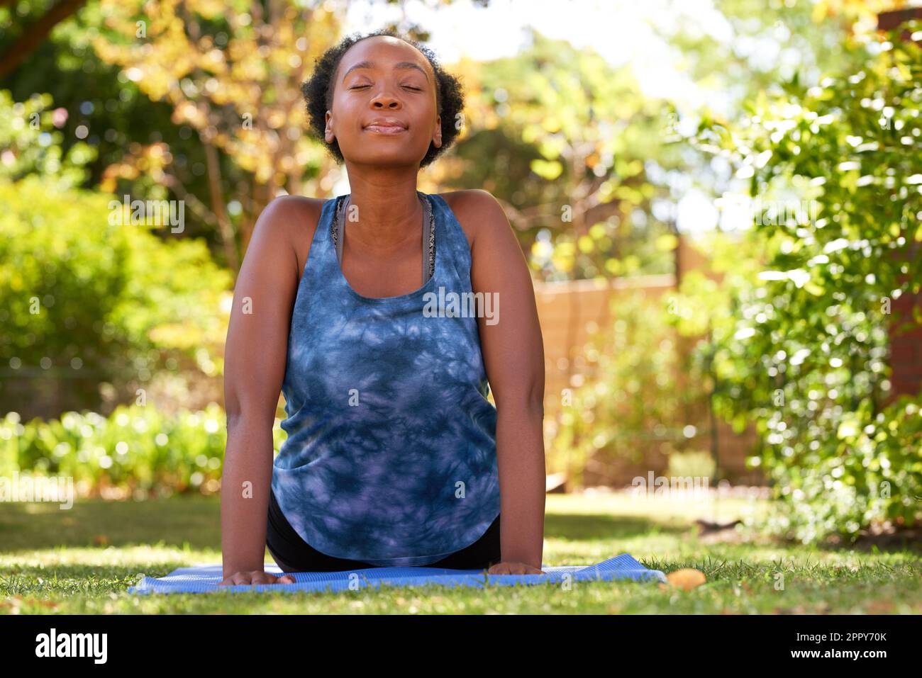 Belle jeune Black Woman fait face vers le haut chien yoga pose à l'extérieur, arbres Banque D'Images