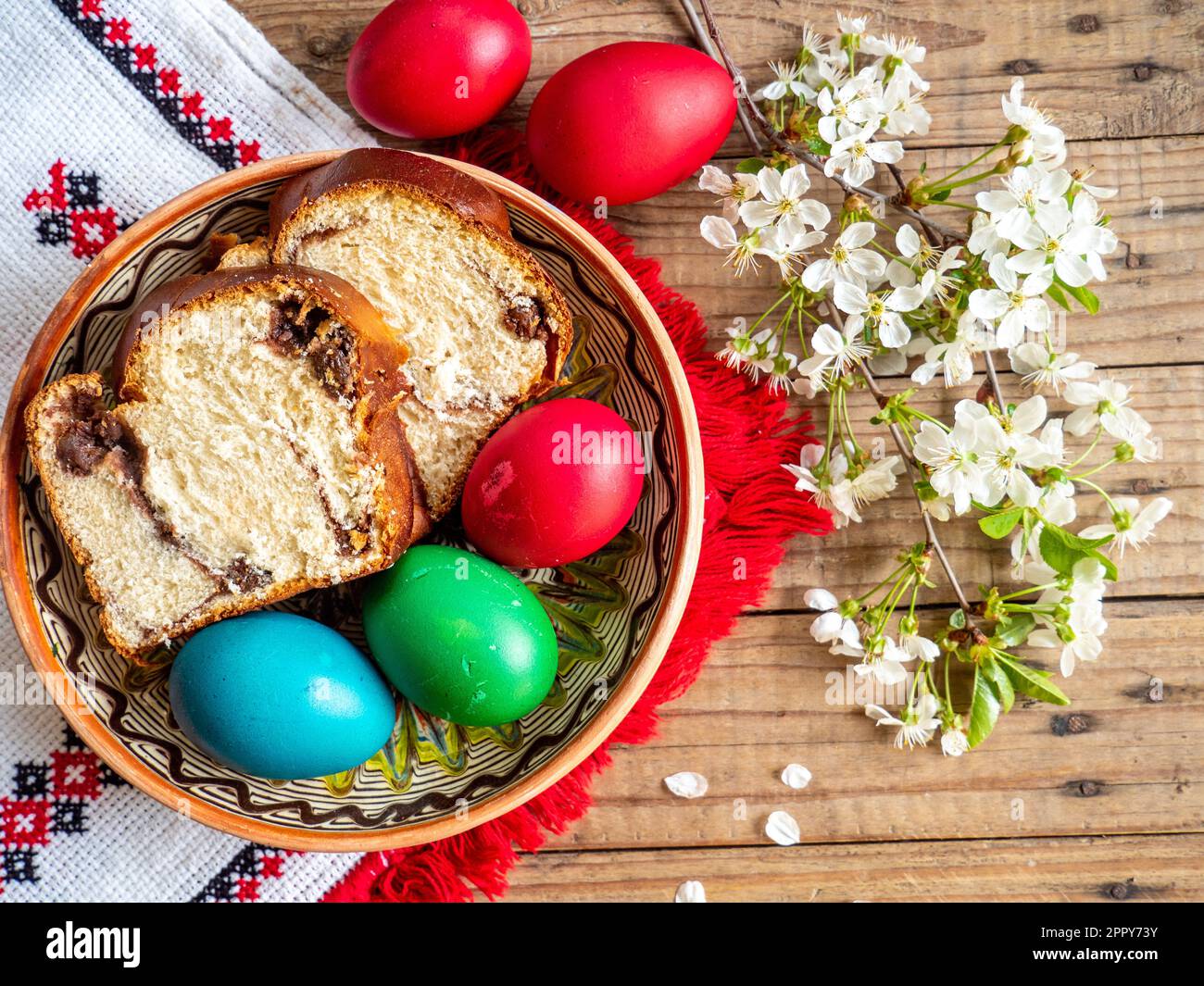 Œufs rouges de Pâques à côté des branches fleuries et assiette avec gâteau doux éponge ou cozonac sur table en bois Banque D'Images