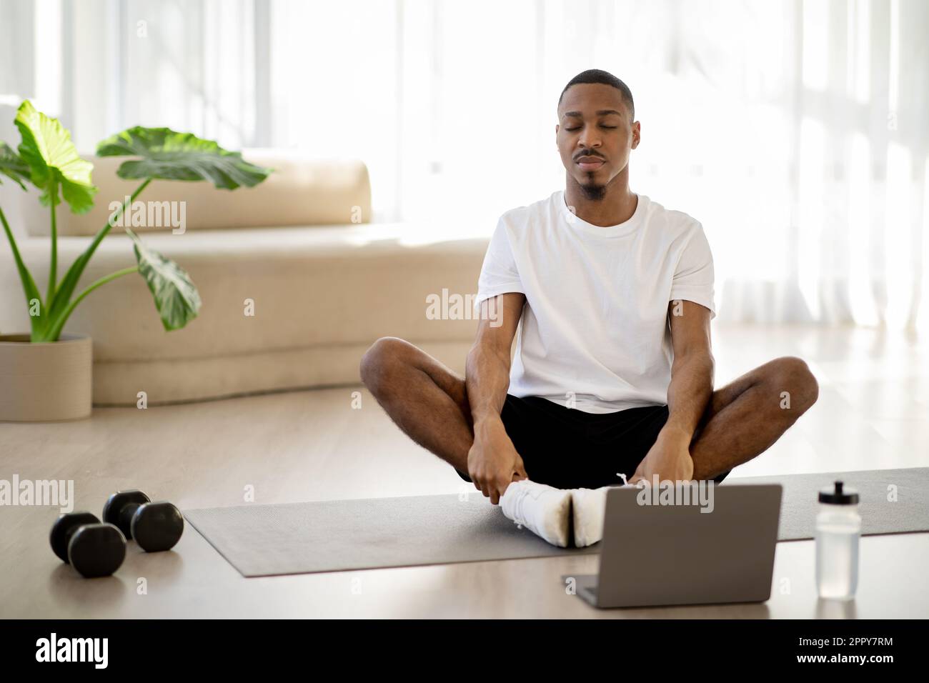 Homme africain paisible méditant à la maison, avoir cours de yoga en ligne Banque D'Images