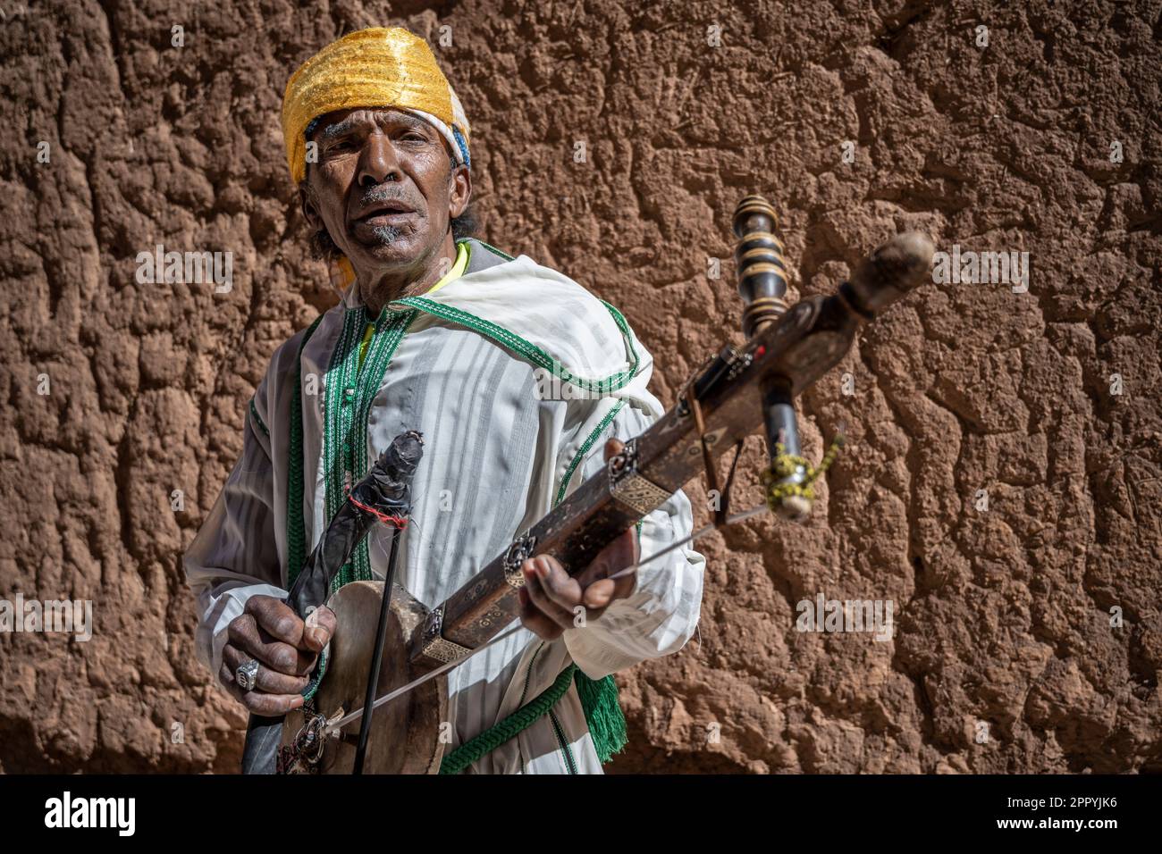 Homme vêtu d'un costume berbère typique jouant un instrument à cordes, connu sous le nom de Ribab, dans les ruelles de la Kasbah Taourirt. Banque D'Images