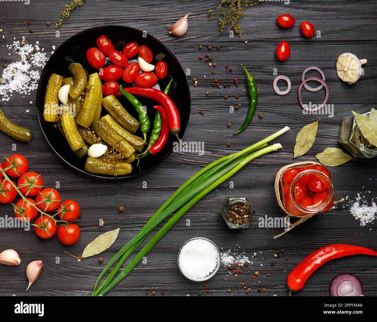 Assortiment de légumes marinés. Tomates en conserve, concombres, piments dans une assiette ronde noire sur fond sombre. apéritif de légumes en conserve. Banque D'Images
